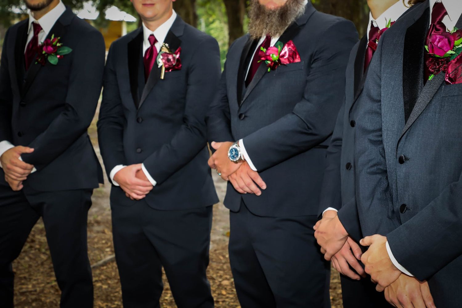 Four groomsmen in dark suits with burgundy boutonnieres standing together at a wedding in High Springs, Florida.