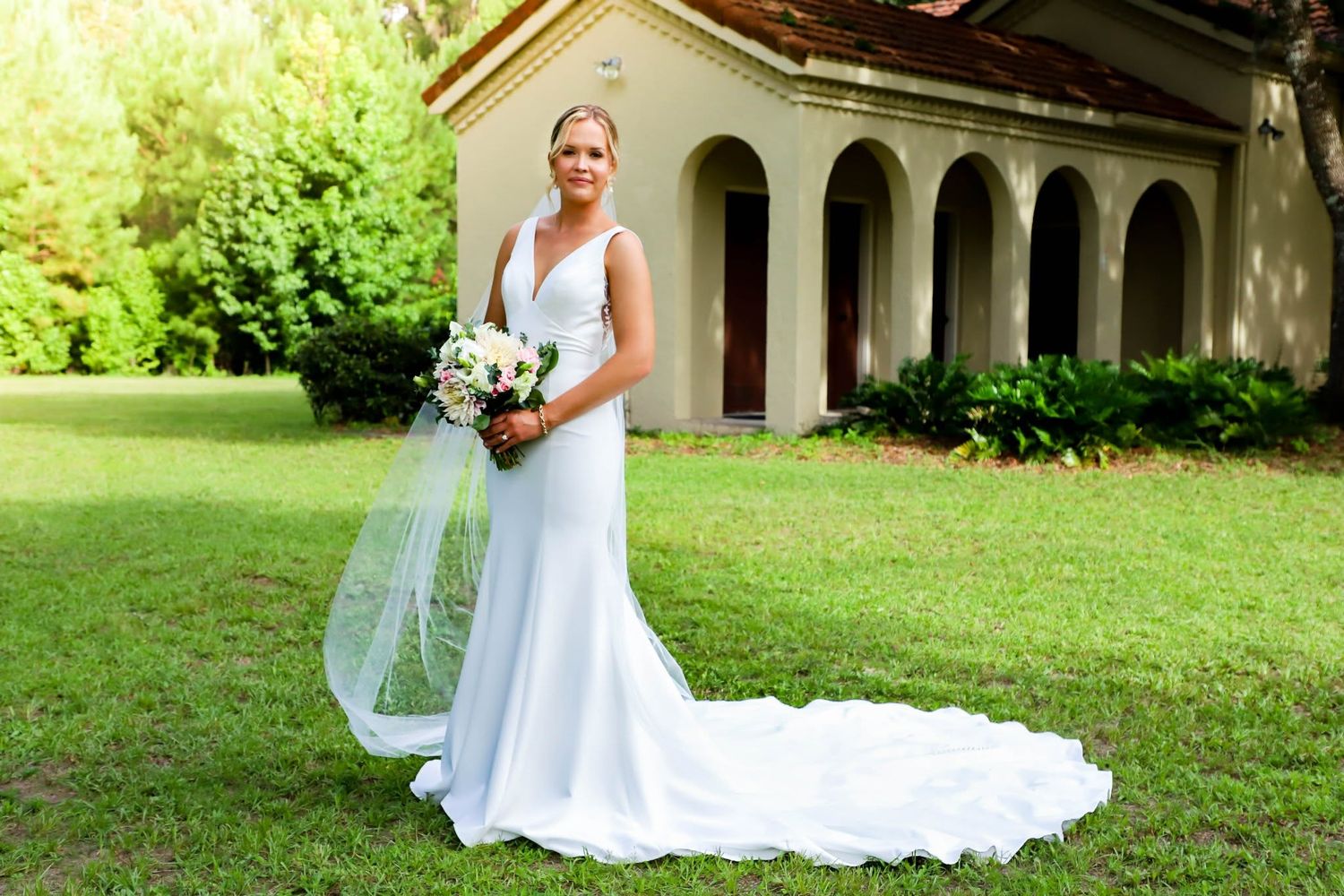 Greek wedding portrait of an elegant bride in a white gown and veil holding a bouquet on a green lawn in Gainesville, Florida.