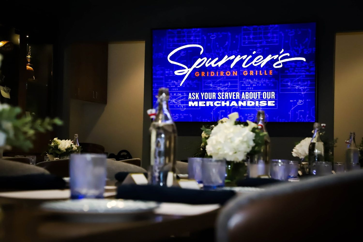 Interior of Spurrier's Gridiron Grille restaurant with elegant table settings and illuminated blue sign.