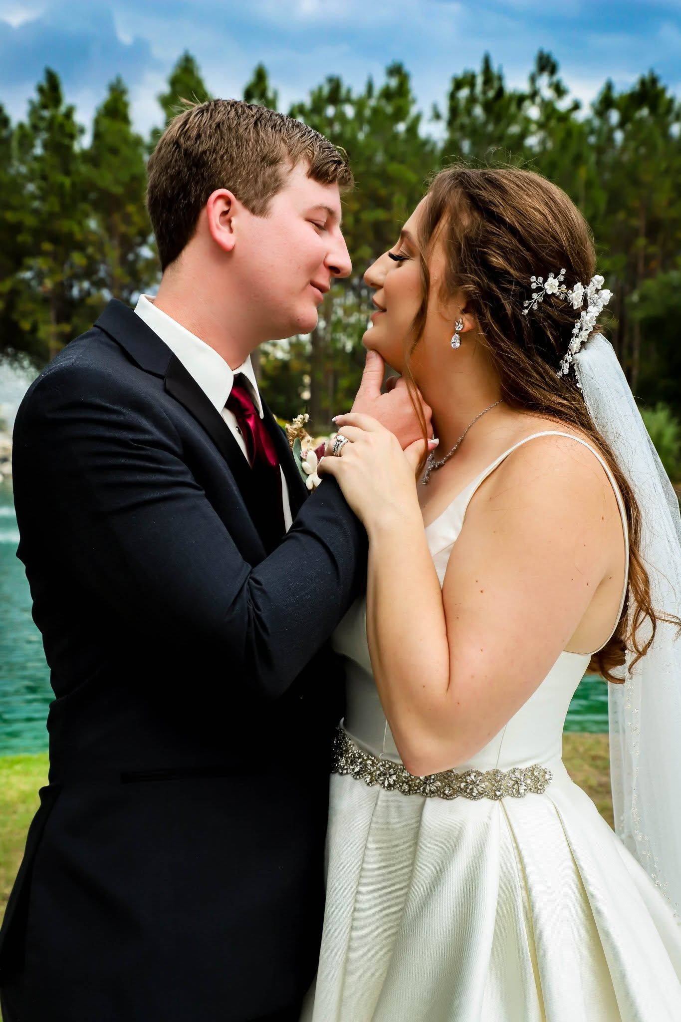A bride and groom share a tender moment, nearly kissing, with a scenic lake and pine trees in the background in Orlando Florida