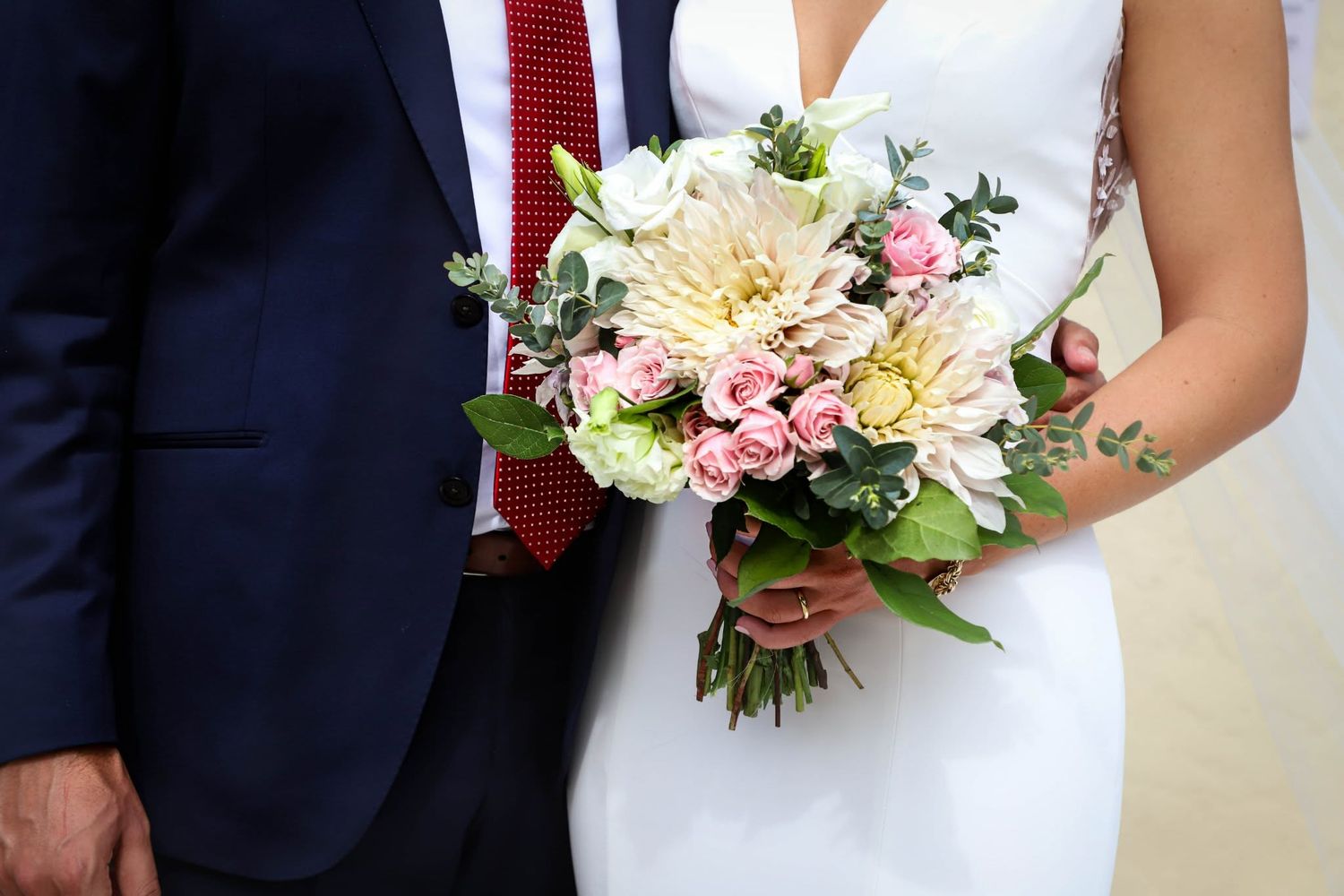 Bride and groom holding white and pink wedding bouquet at ceremony.