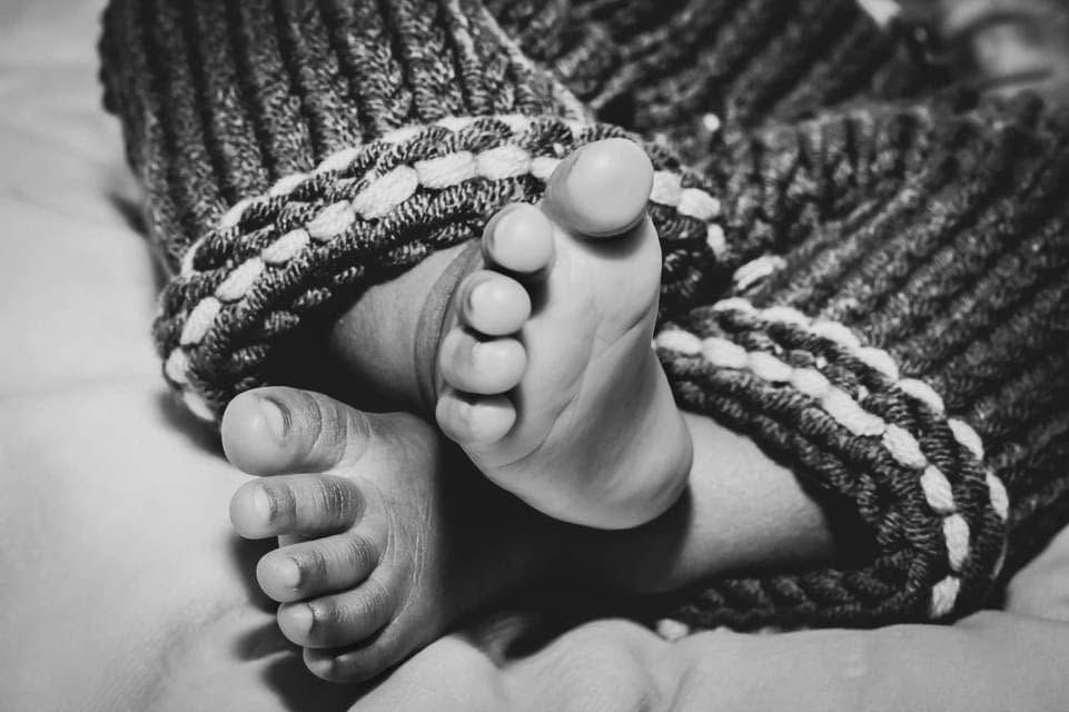 Black and white close-up of newborn baby feet wrapped in cozy knitted blanket.