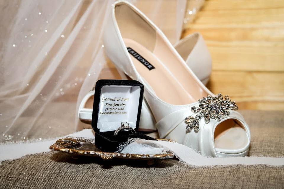 Wedding detail photo featuring white bridal heels with a crystal brooch, Tiffany jewelry box, and bridal accessories arranged on burlap in H