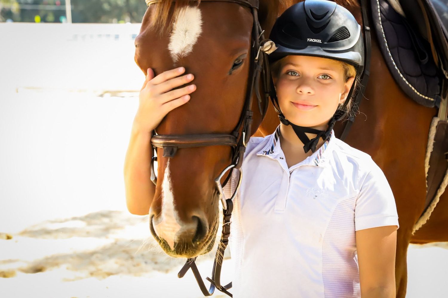 Young equestrian rider in a helmet stands beside a brown horse in an outdoor riding arena in Gainesville, Florida.