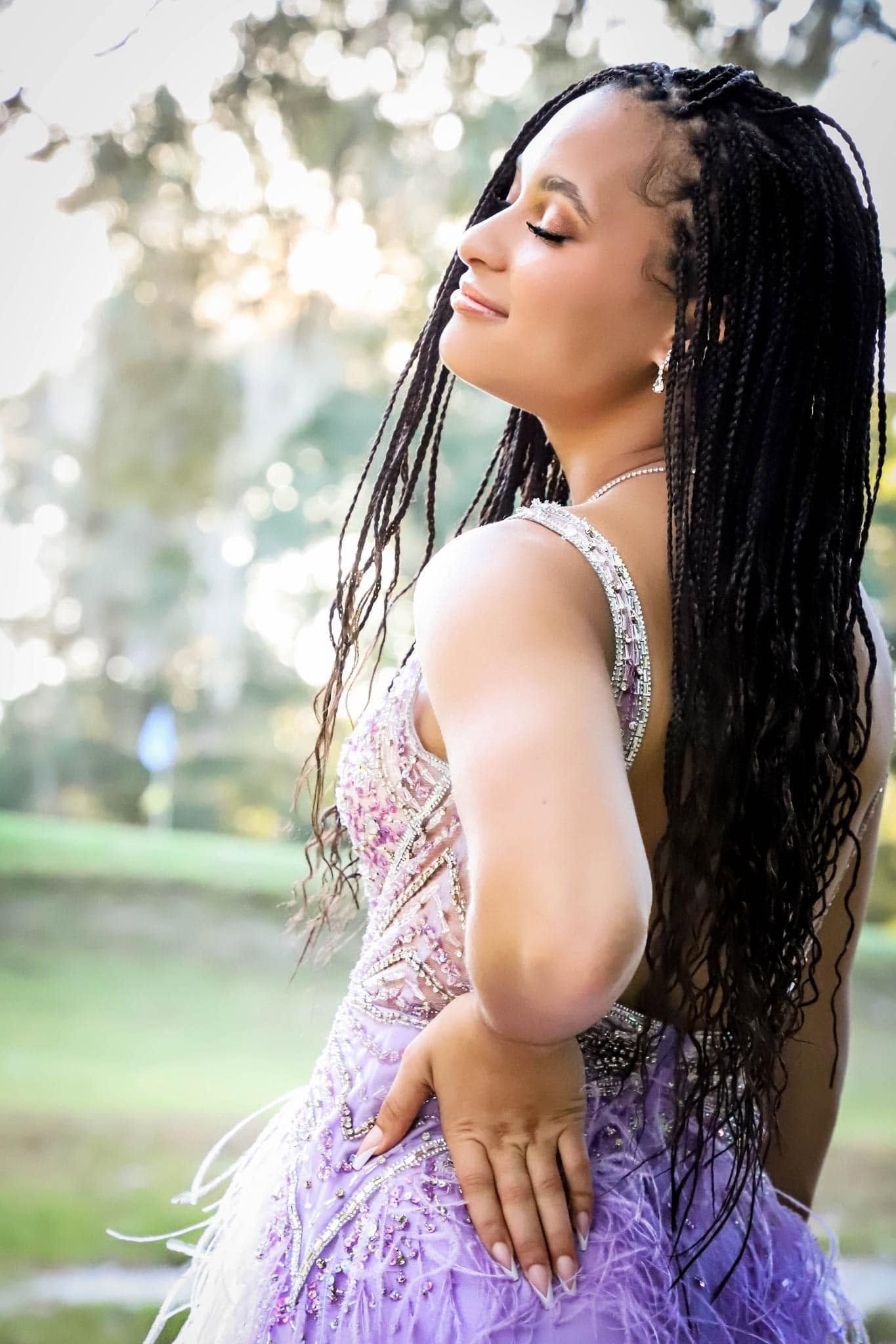 Prom portrait of a young woman with long hair wearing a lavender feathered dress, posing outdoors during golden hour in Alachua, Florida