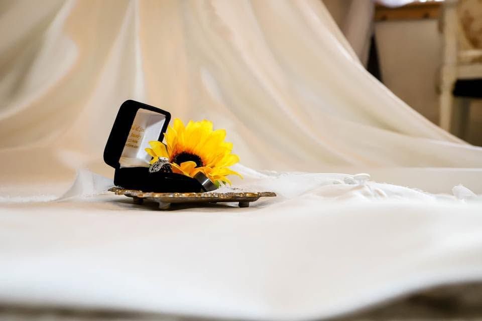 Elegant wedding ring box with yellow sunflower decoration displayed on white bridal veil fabric.