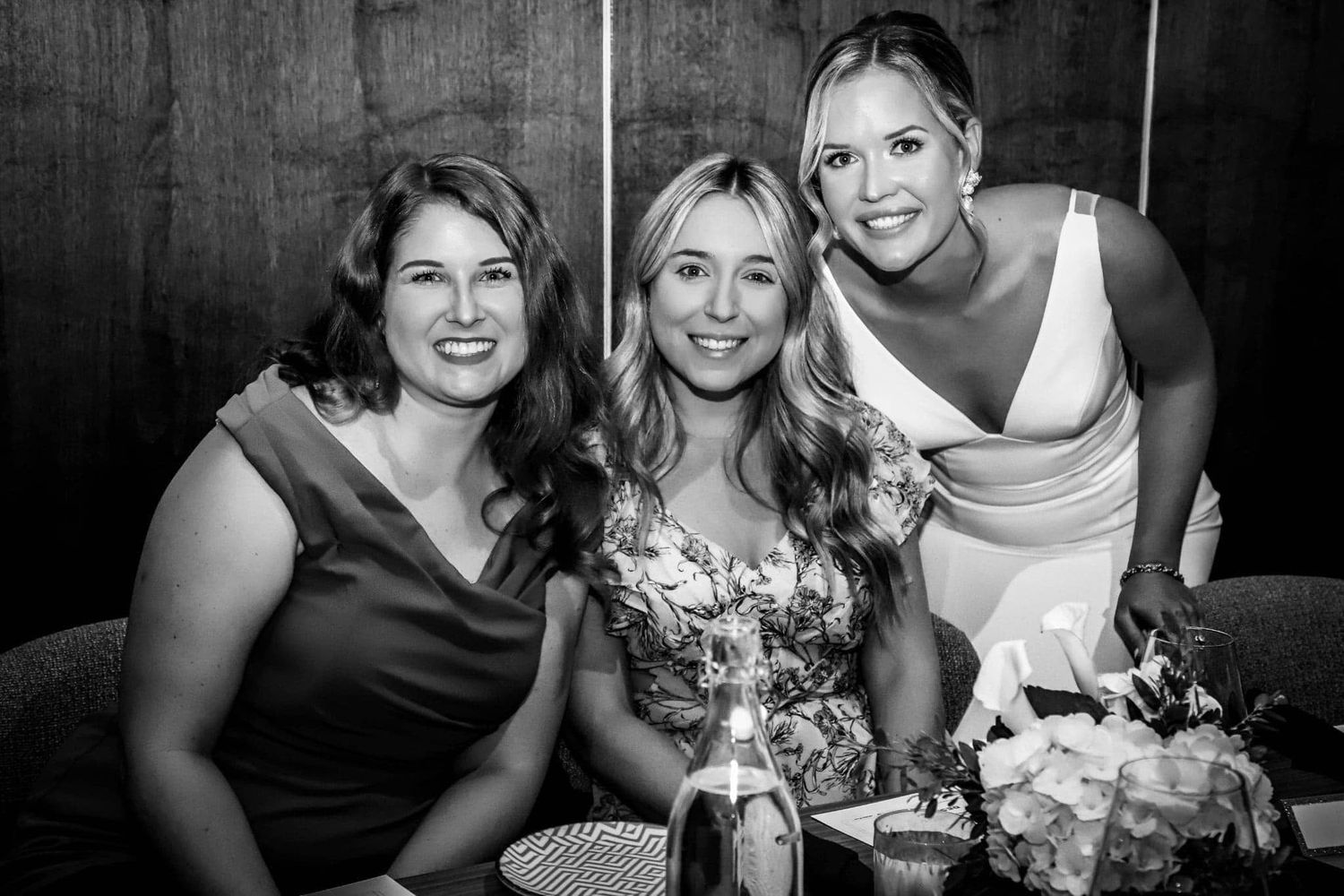 Three women smile together at an event in a black and white portrait photo.
