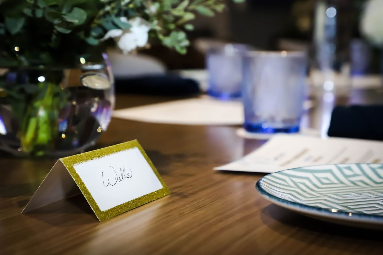 Gold glitter place card on wooden table at elegant wedding reception.