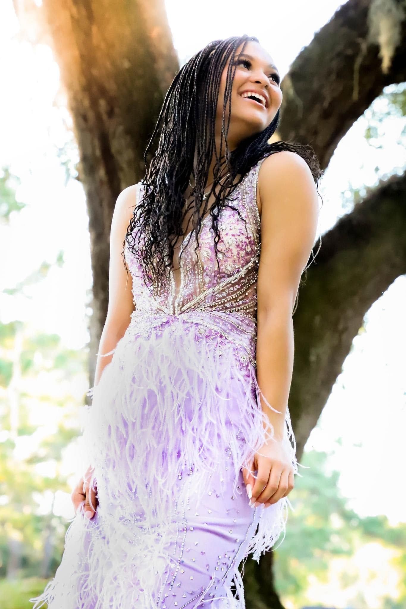 Portrait of a young woman in a lavender feathered gown posing beside a large oak tree in Gainesville, Florida.