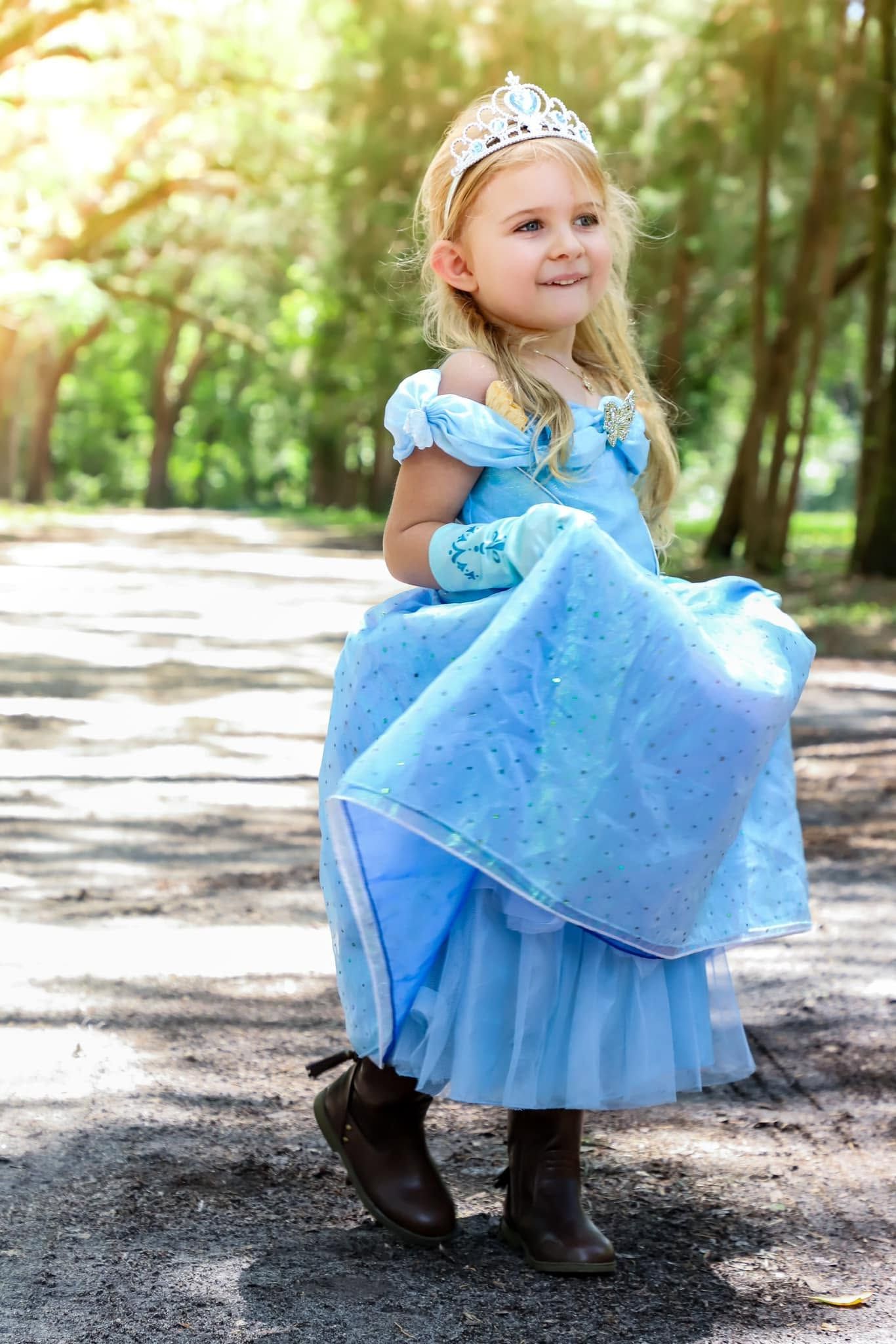 A little girl in a blue Cinderella princess dress and crown twirls on an outdoor path in Stark Florida