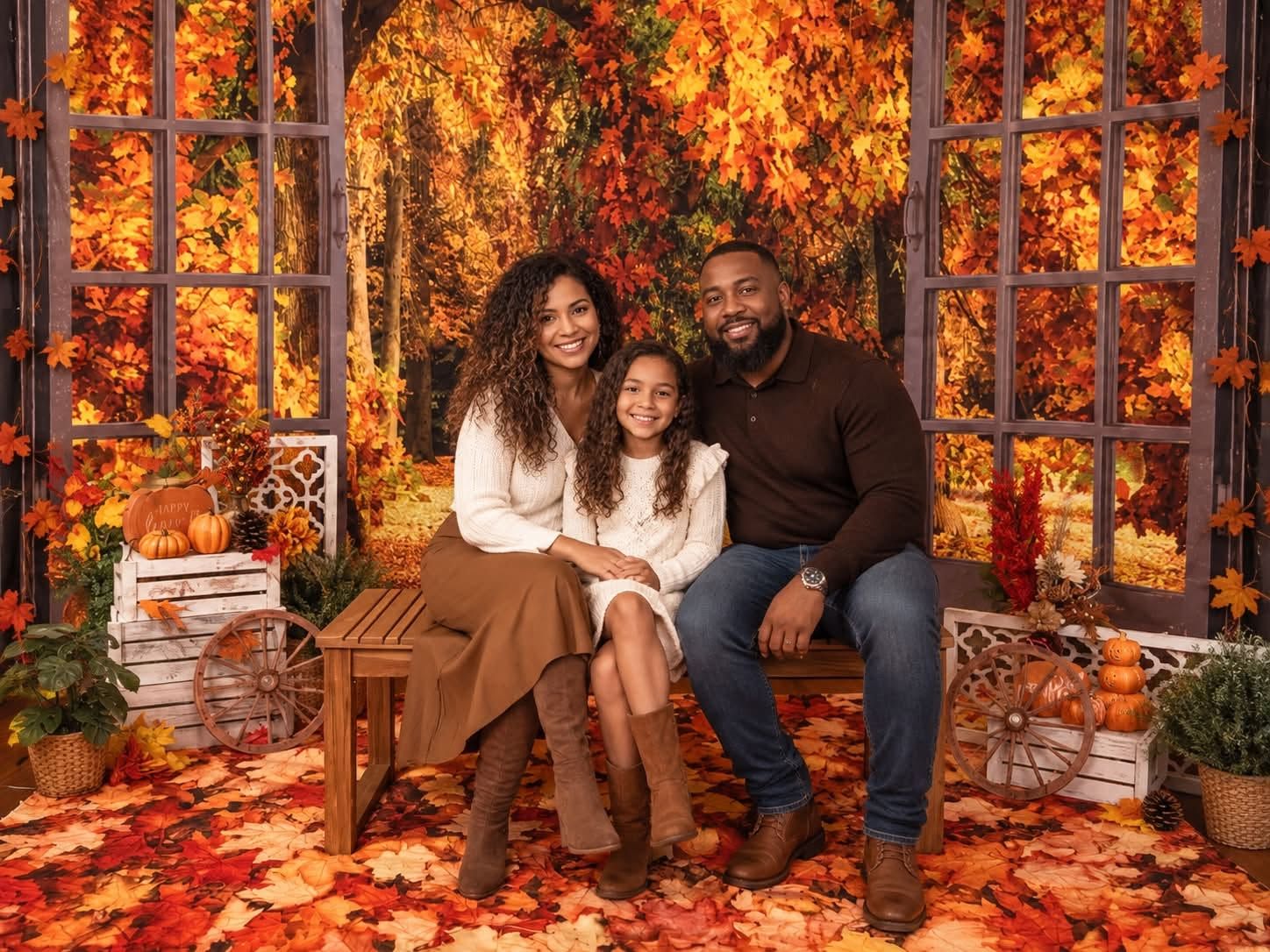 A family of three poses together in front of a vibrant autumn foliage backdrop with pumpkins.