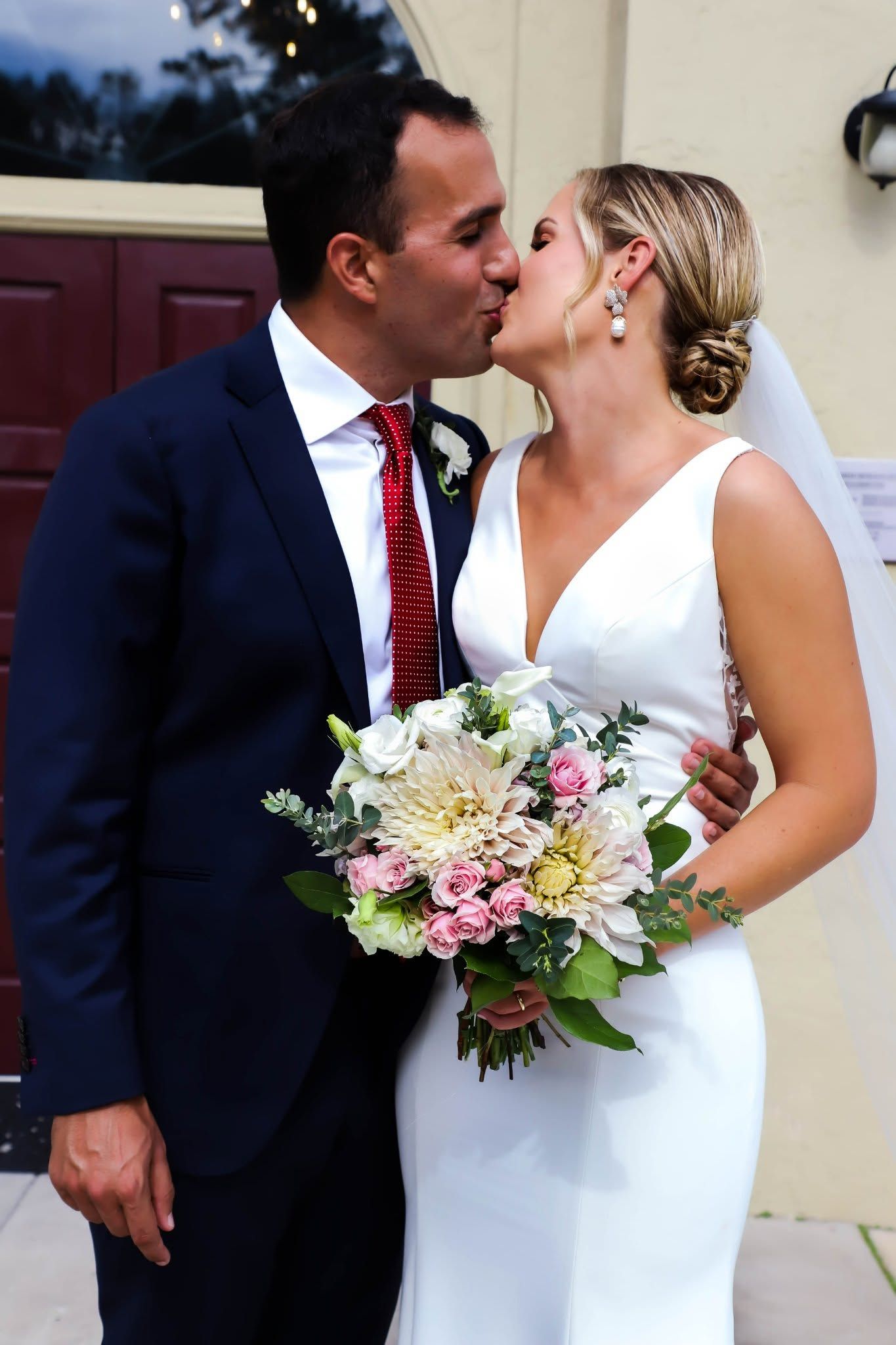 Bride and groom share a romantic kiss while holding a pastel wedding bouquet in Jacksonville, Florida.