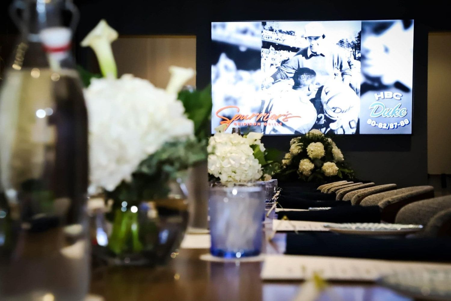Elegant event table display with white floral arrangements and vintage black and white photo on screen.