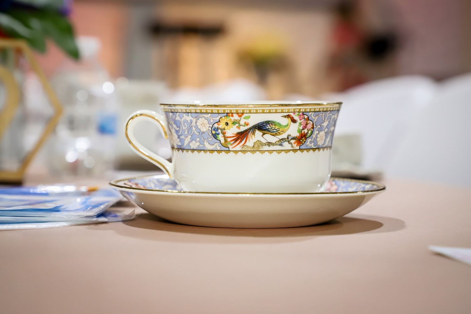 Ornate fine china teacup and saucer with colorful bird design displayed on elegant table setting.