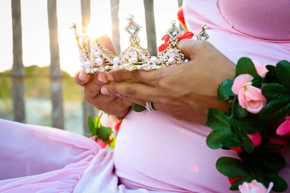 Maternity session with pregnant woman in pink dress holding a crown and roses in soft sunlight in Georgia.