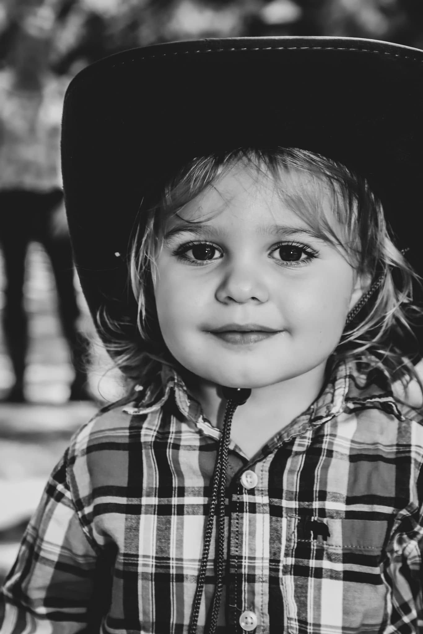 Black and white portrait of a toddler wearing a cowboy hat and plaid shirt.