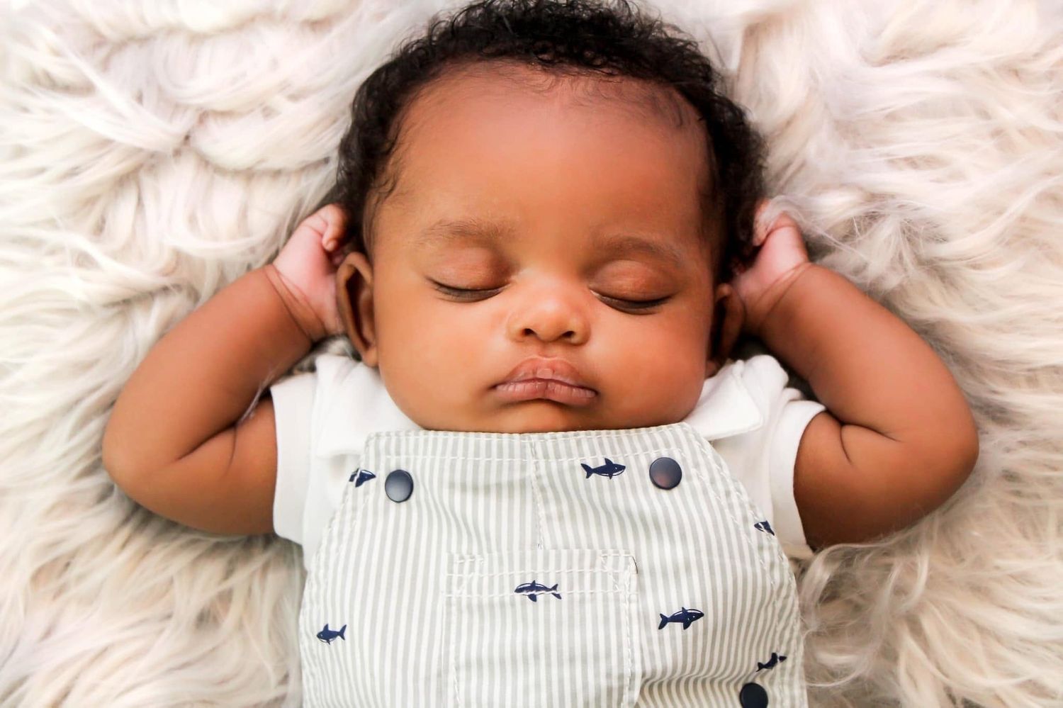 Peaceful newborn baby sleeping on fluffy white blanket in striped onesie.