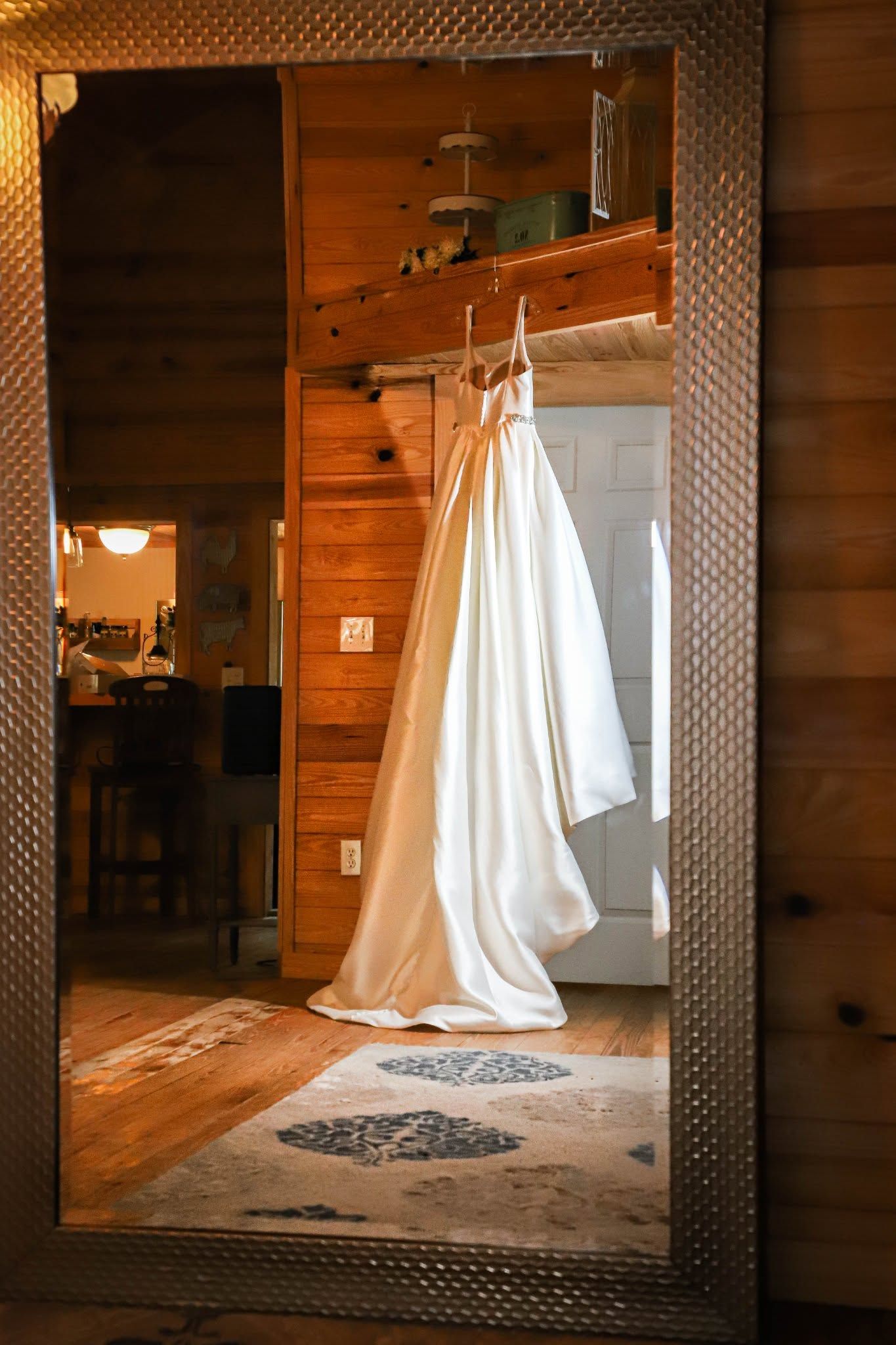 A white wedding gown hangs in a rustic wooden cabin reflected in a decorative mirror in Highsprings Florida