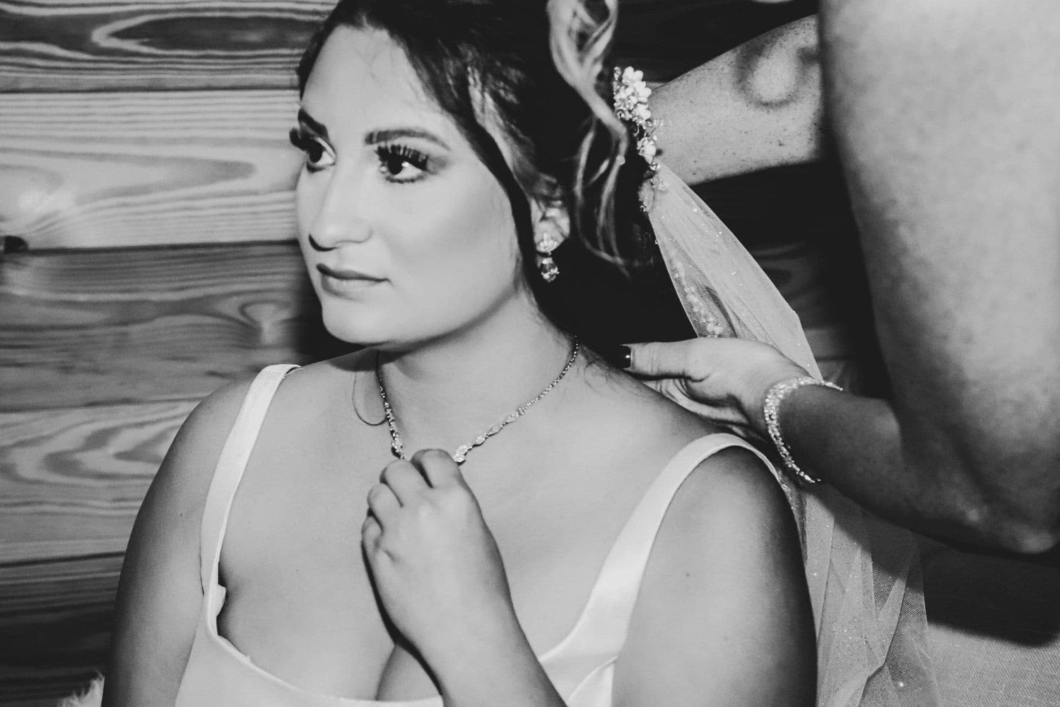 Black and white wedding photo of a bride having her necklace fastened while wearing a veil in High Springs, Florida