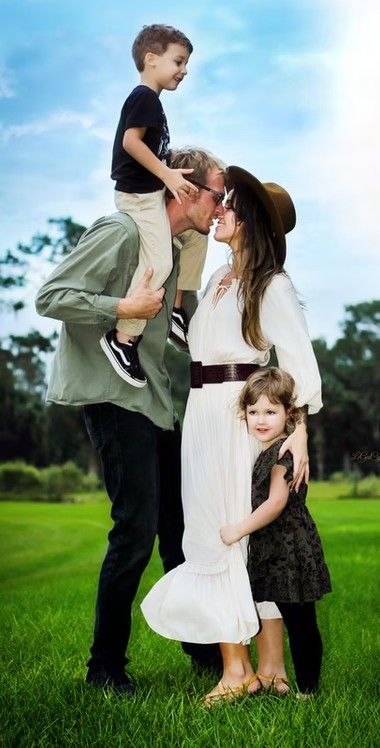 A couple shares a kiss while their two young children play around them on a green lawn.