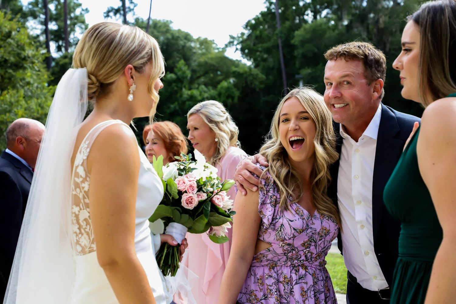 Excited wedding guests greeting the bride outdoors after the ceremony in a garden setting.