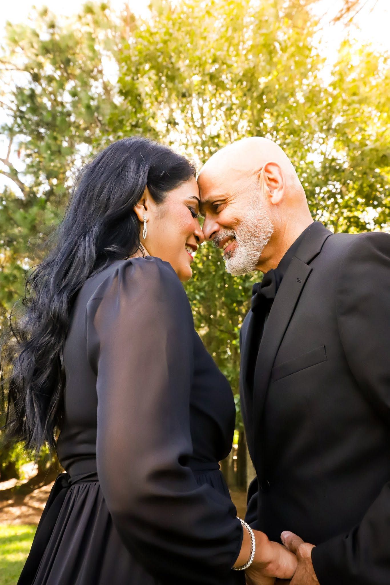 Couple in black outfits touch foreheads and hold hands in a sunlit garden in Ocala, Florida.