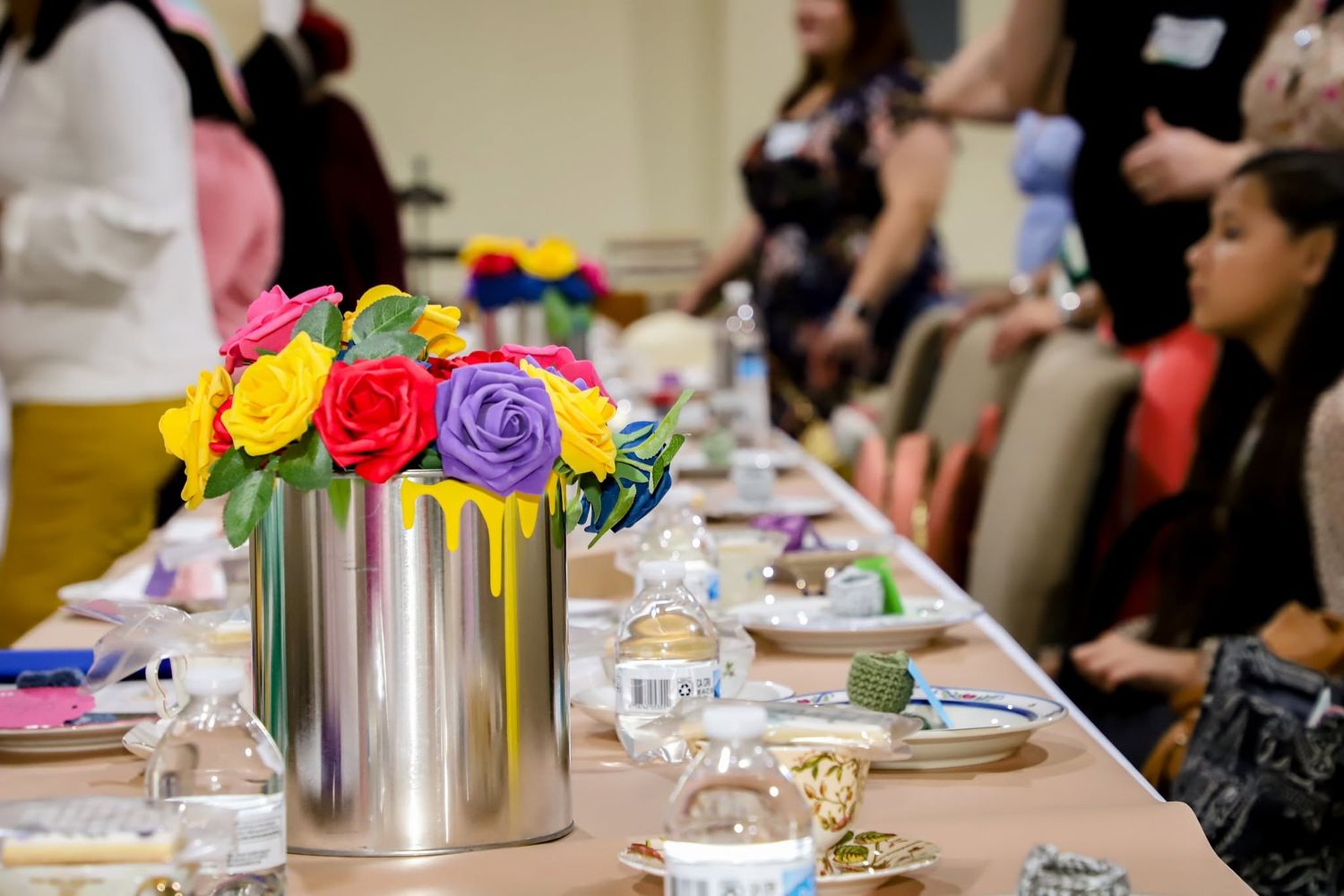 All woman's event in Savannah Georgia. Colorful paper roses in silver paint can vase centerpiece on elegantly set banquet table.