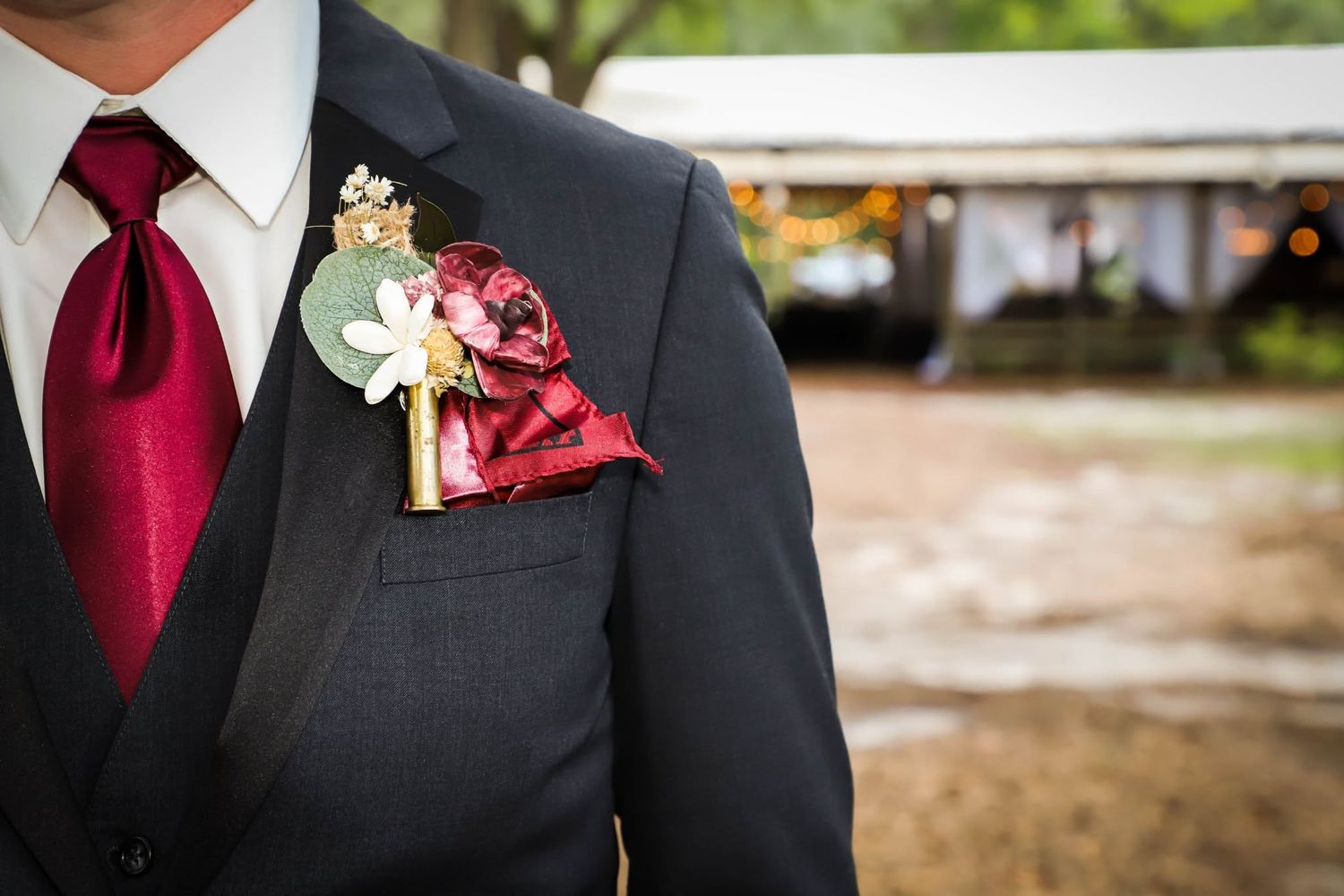 Groom in dark suit with burgundy tie and floral boutonniere at wedding.