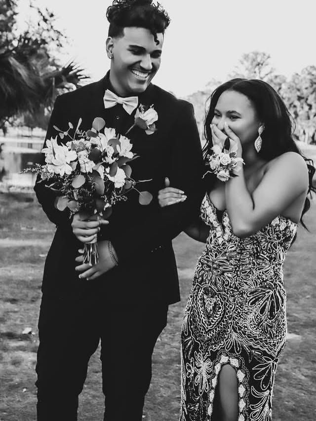 Senior Home Coming in Gainesville Florida. Laughing couple in black and white photo, man in tuxedo holds bouquet at outdoor prom event.