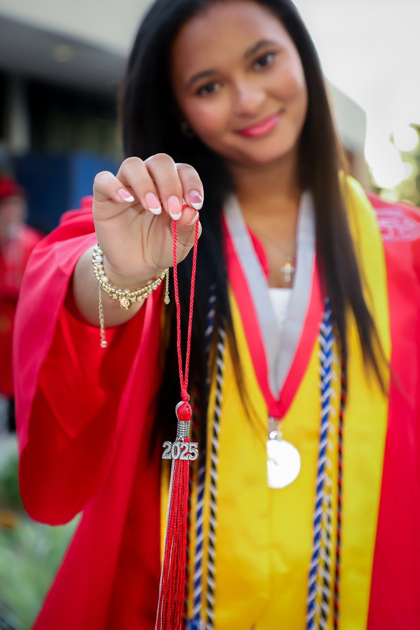 Gainesville Florida Senior Graduation. Smiling graduate in red cap and gown holds up class of 2025 tassel necklace at graduation.