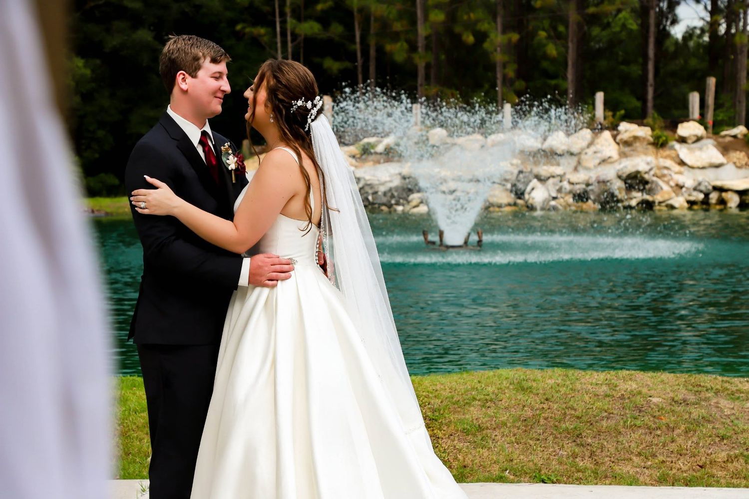 Bride and groom embracing near fountain at outdoor wedding venue.