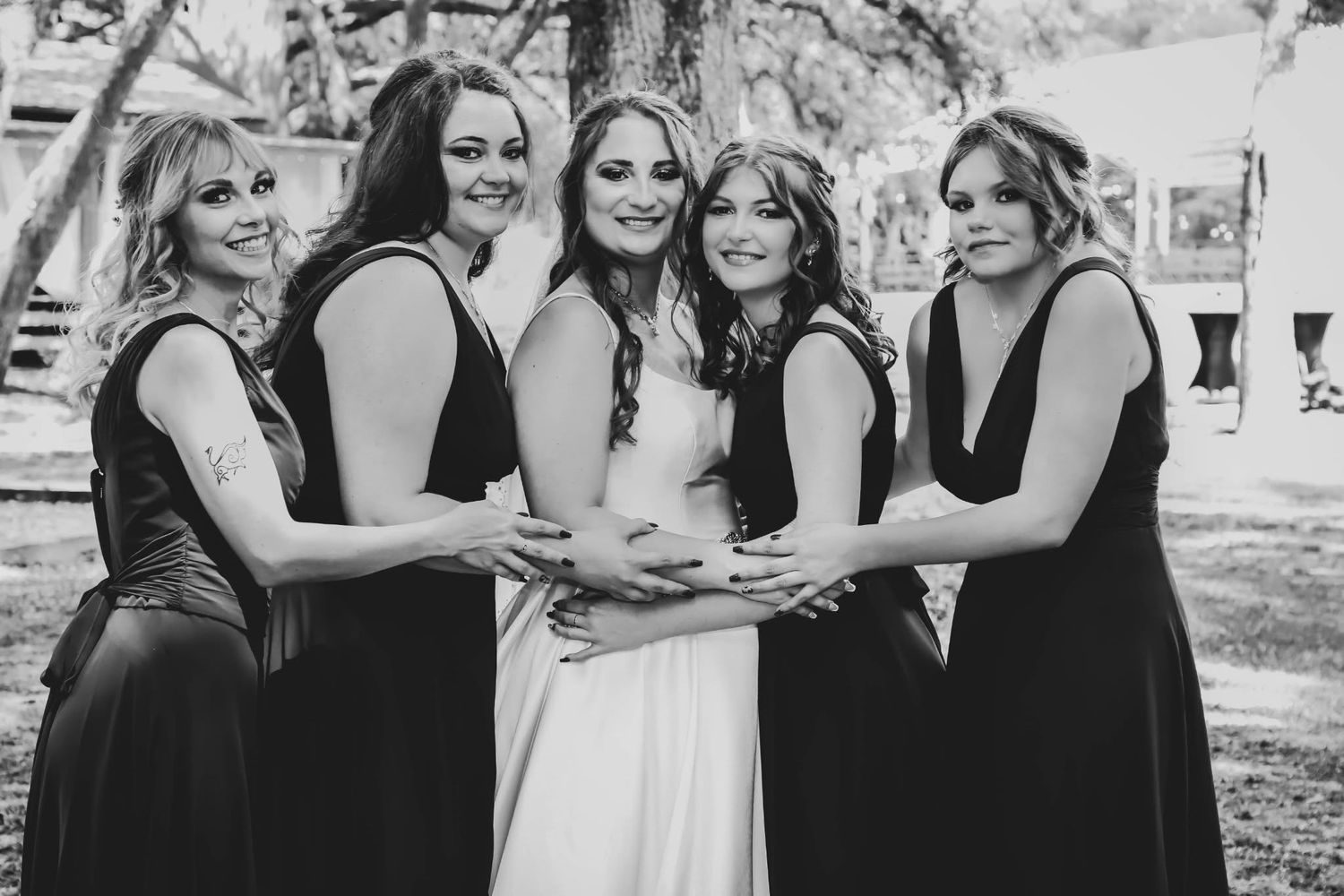 Bride in white gown with four bridesmaids in black dresses posing together in black and white photo.
