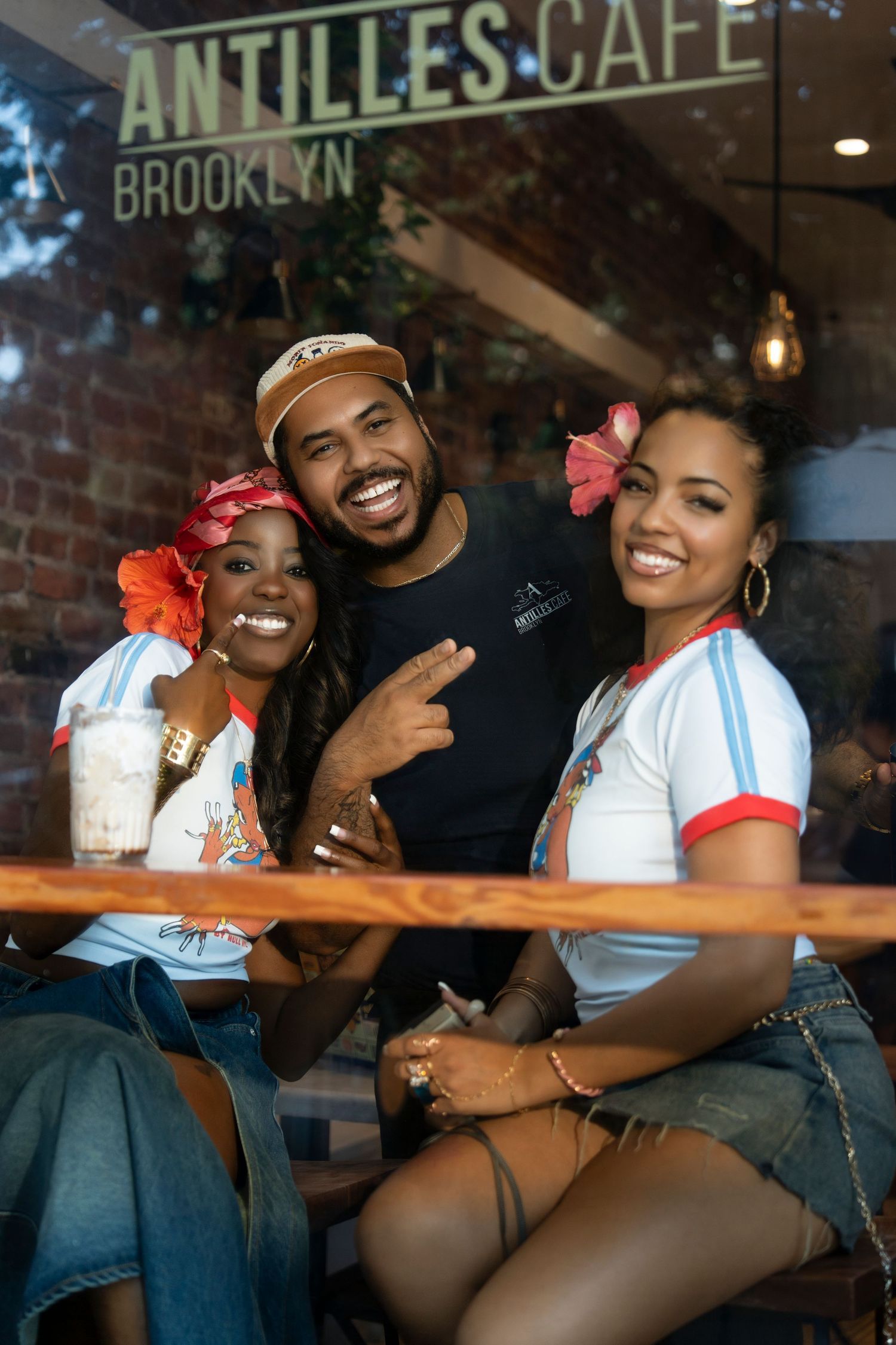 Three friends smiling and posing together outside Antilles Cafe Brooklyn on a sunny day.