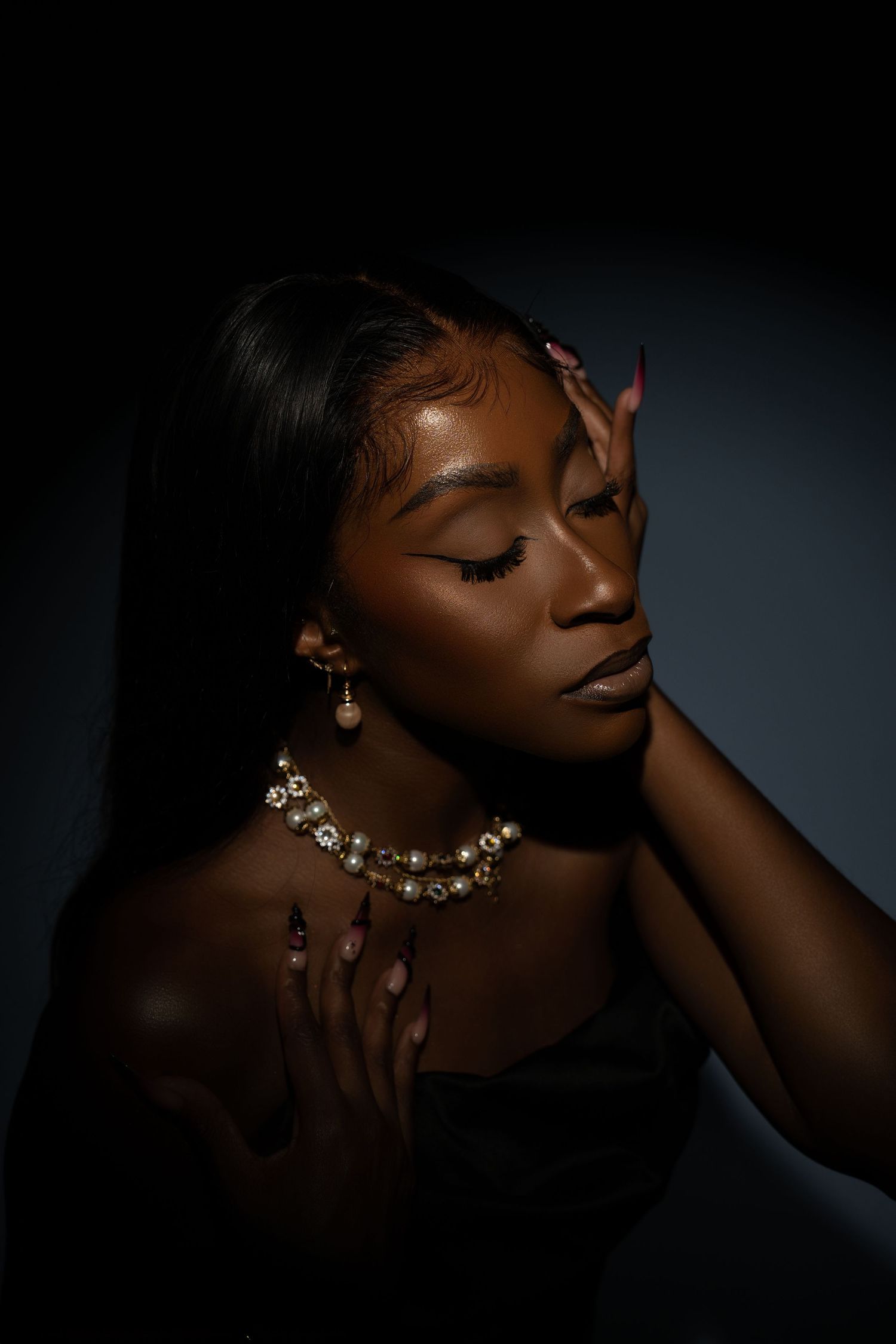 Close-up portrait of woman with pearl necklace in dramatic dark lighting.