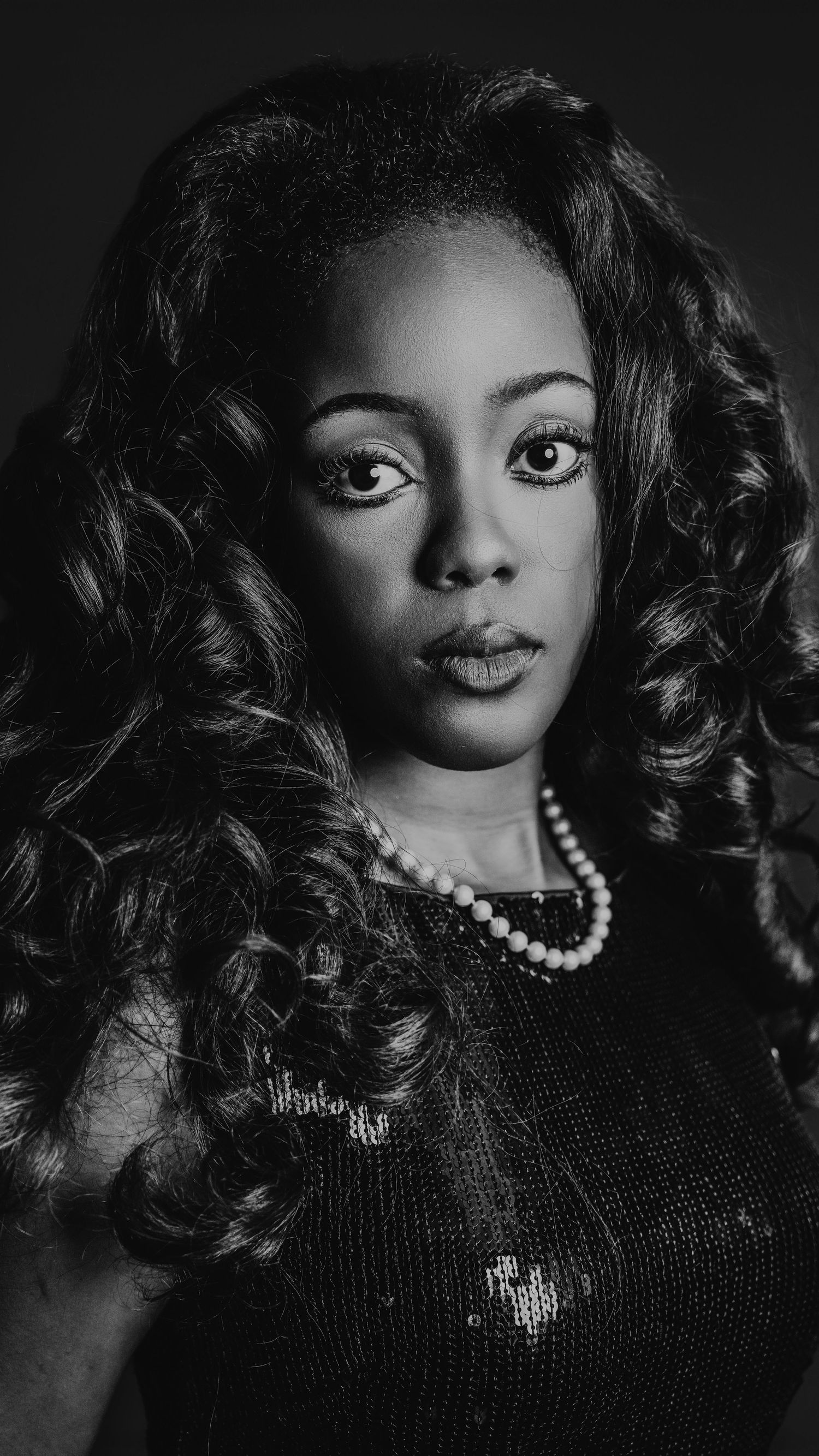 Dramatic black and white portrait of woman with curly hair and pearls.