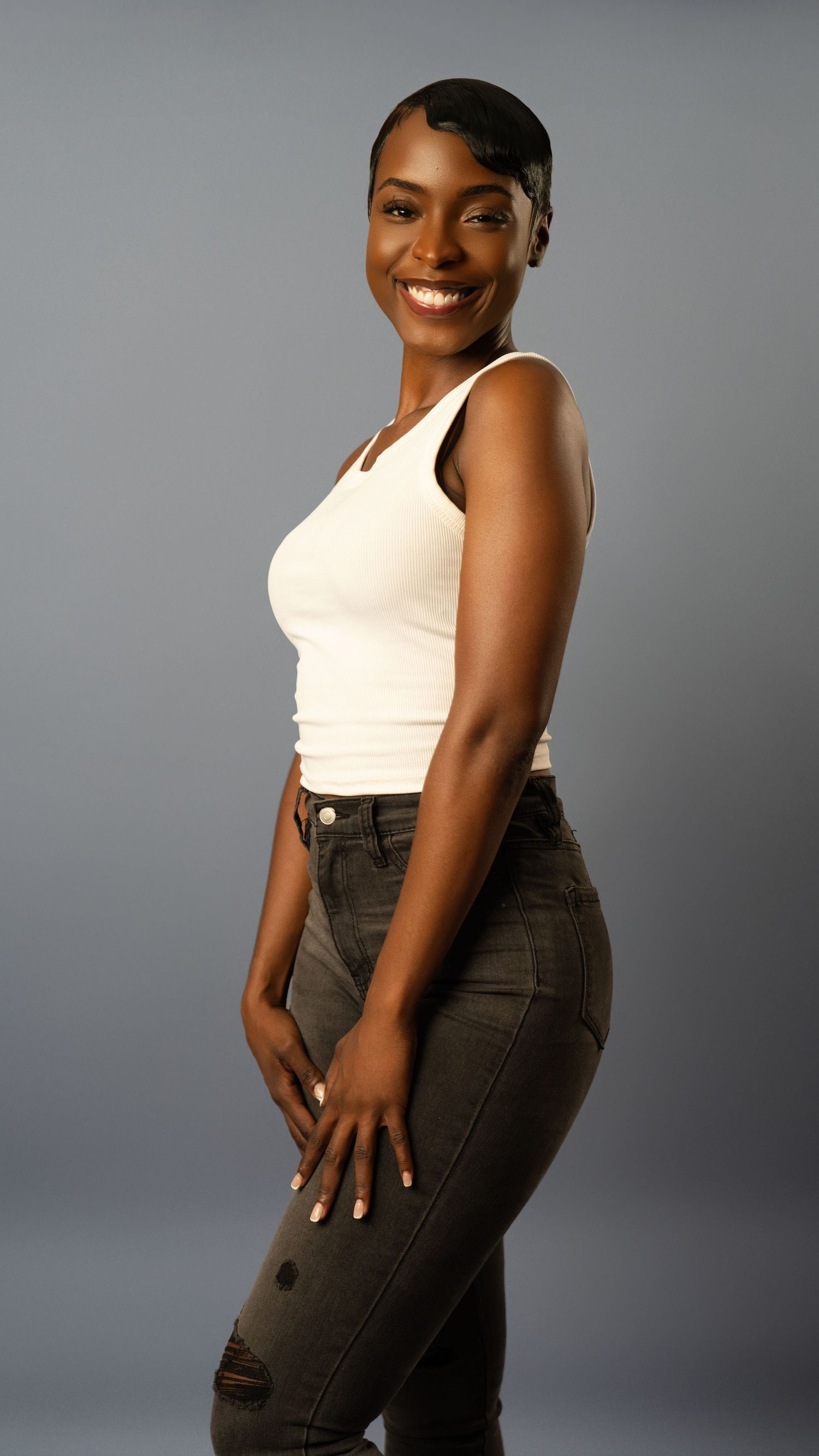 Smiling woman in white crop top and dark distressed jeans poses sideways in photography studio.