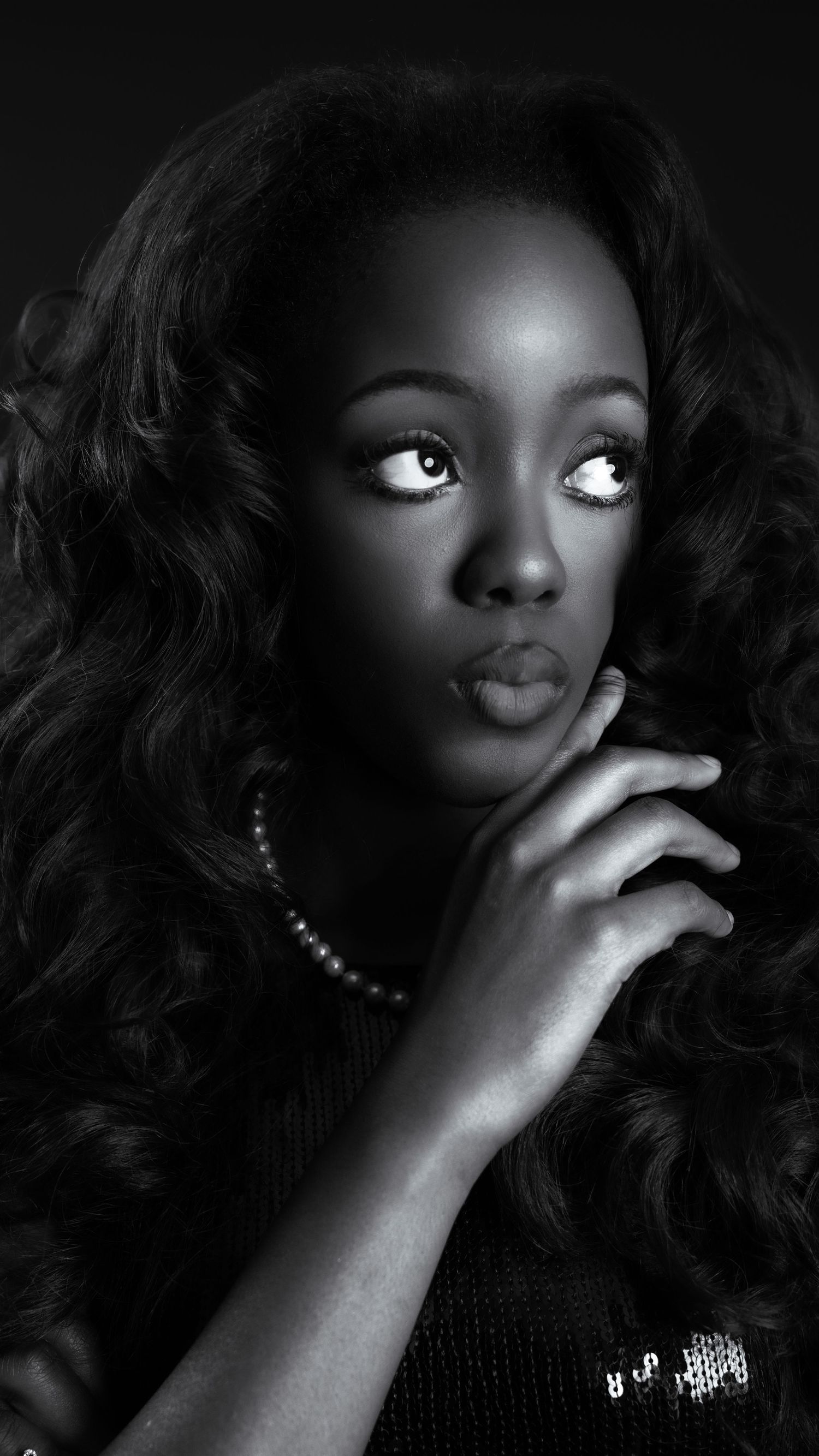 Striking black and white portrait of Black woman with voluminous curly hair and pearl necklace.