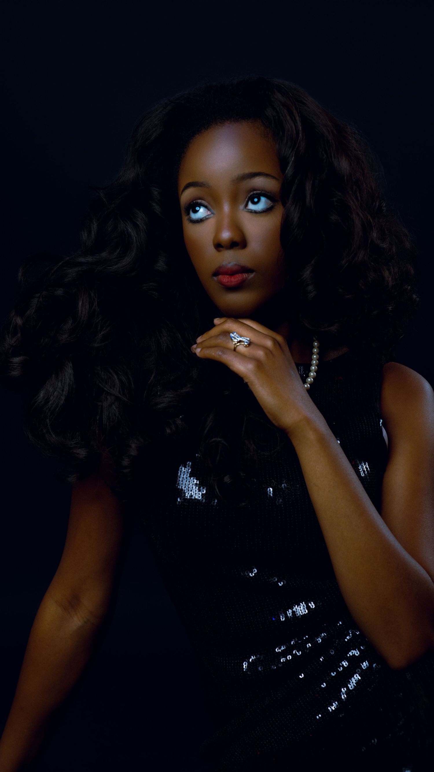 Glamorous woman in sequin top with pearl necklace and voluminous curls.