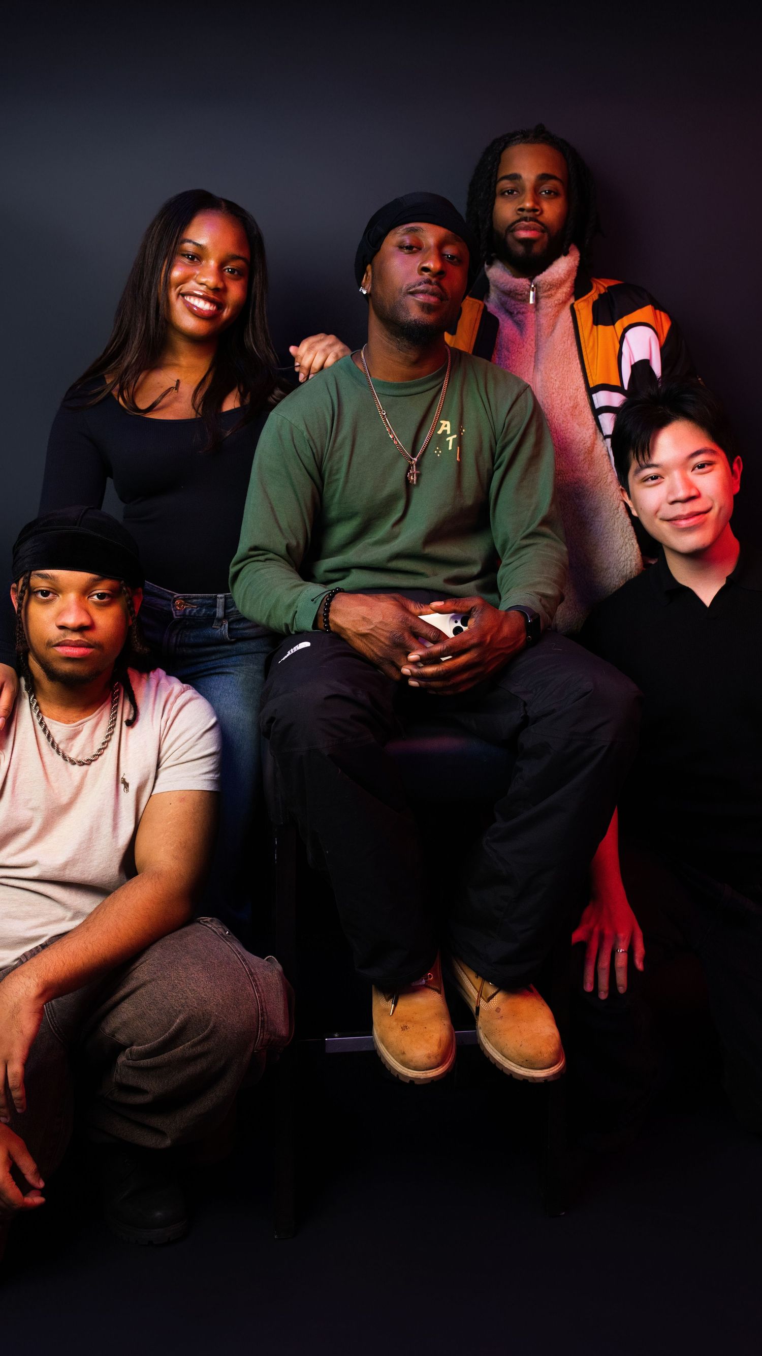 Five young adults pose together for a group portrait photo against a dark studio background.