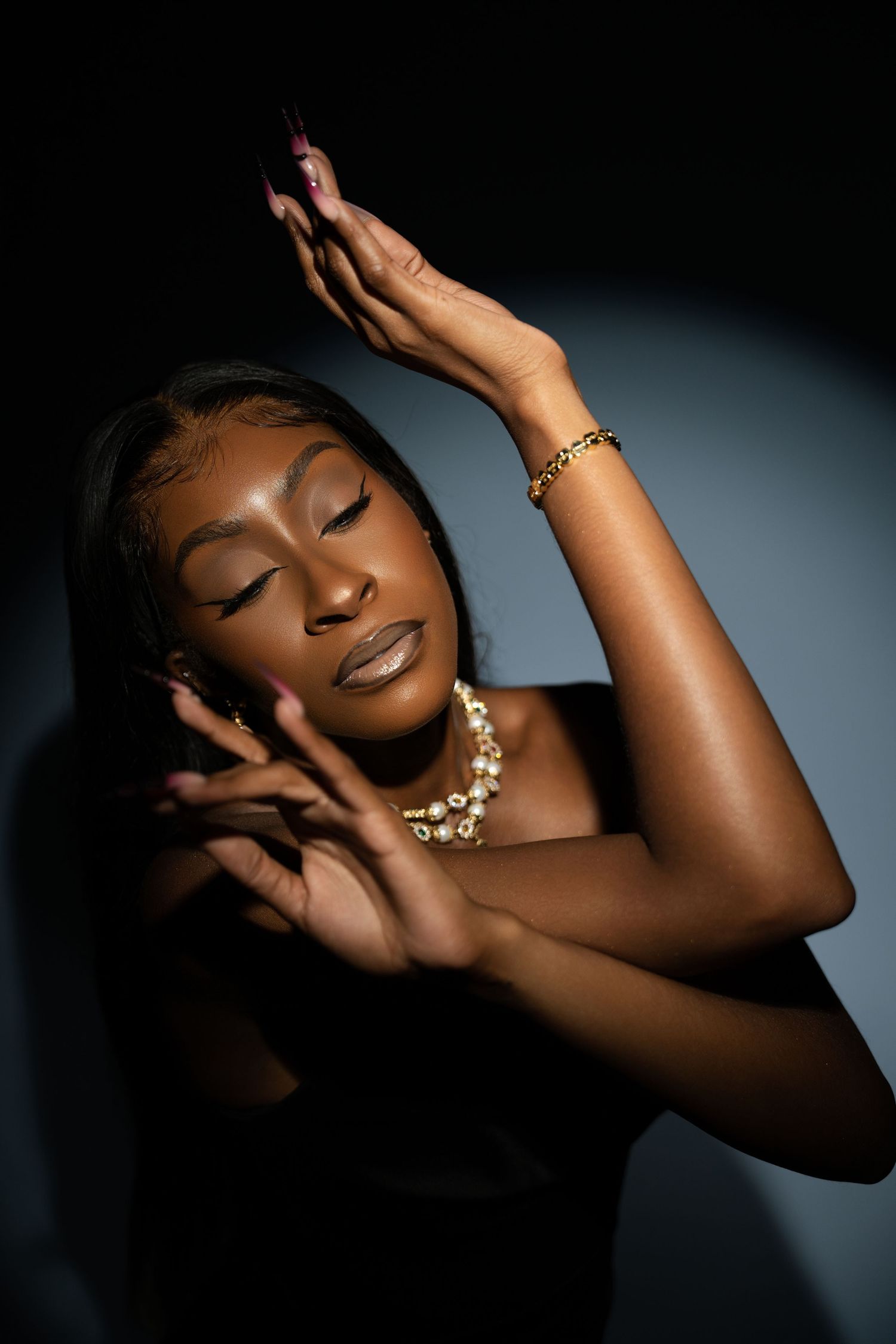 Woman in black strapless dress poses with raised hands in shadow light.