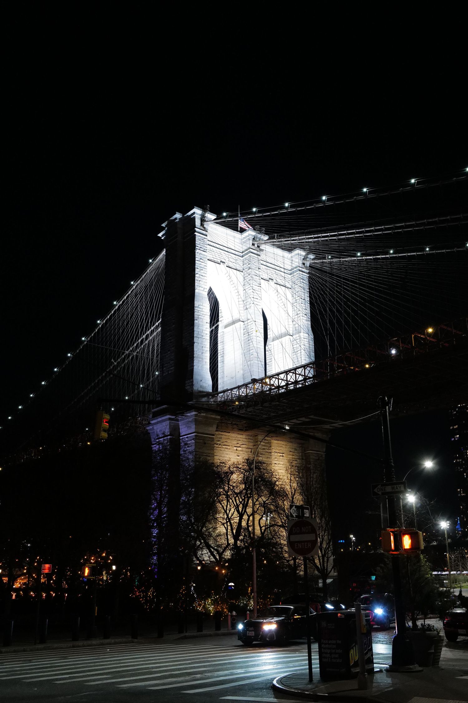 Brooklyn Bridge tower lit up dramatically against night sky.