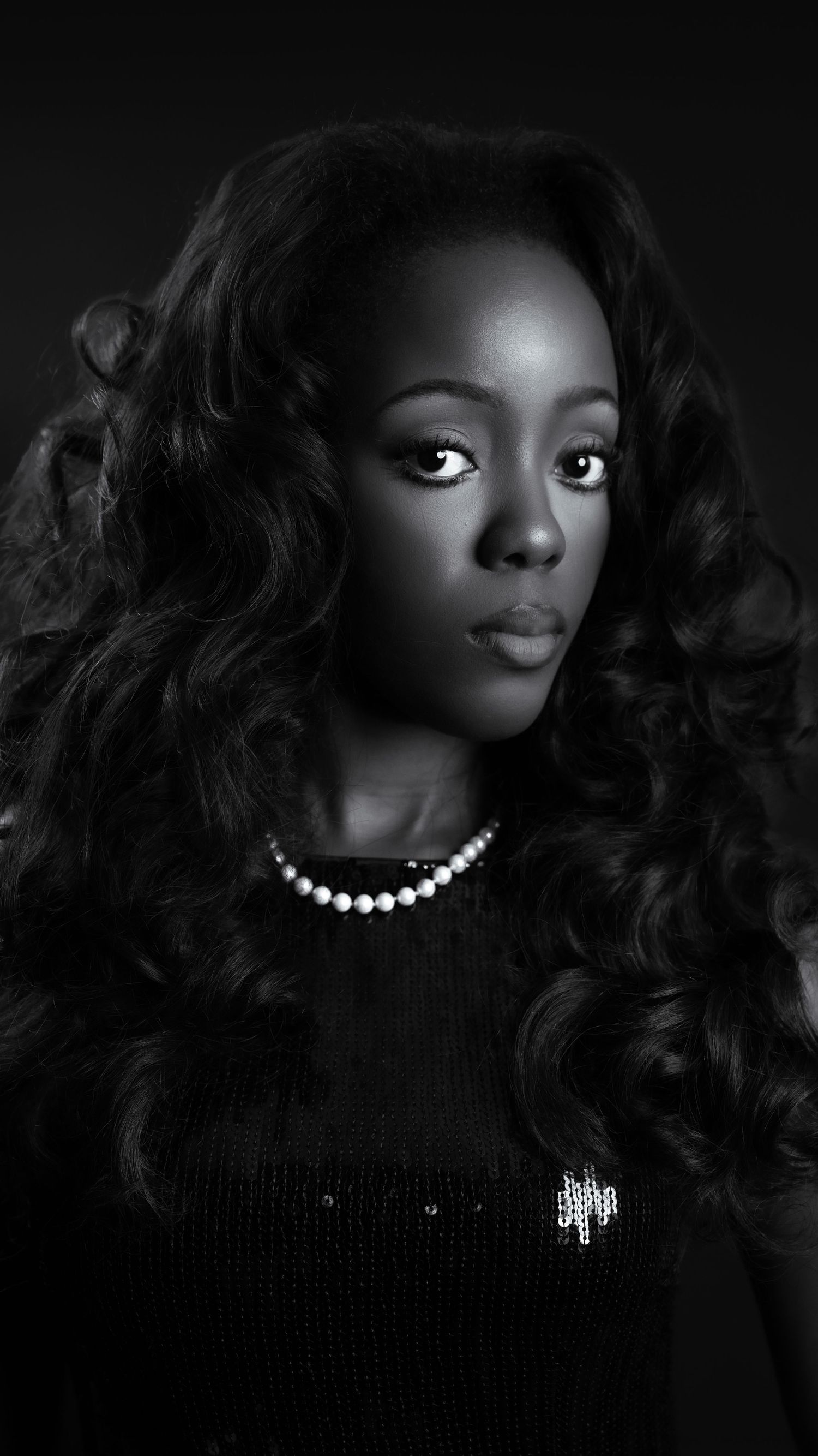 Elegant black and white close-up portrait of Black woman with curly hair and pearl necklace.
