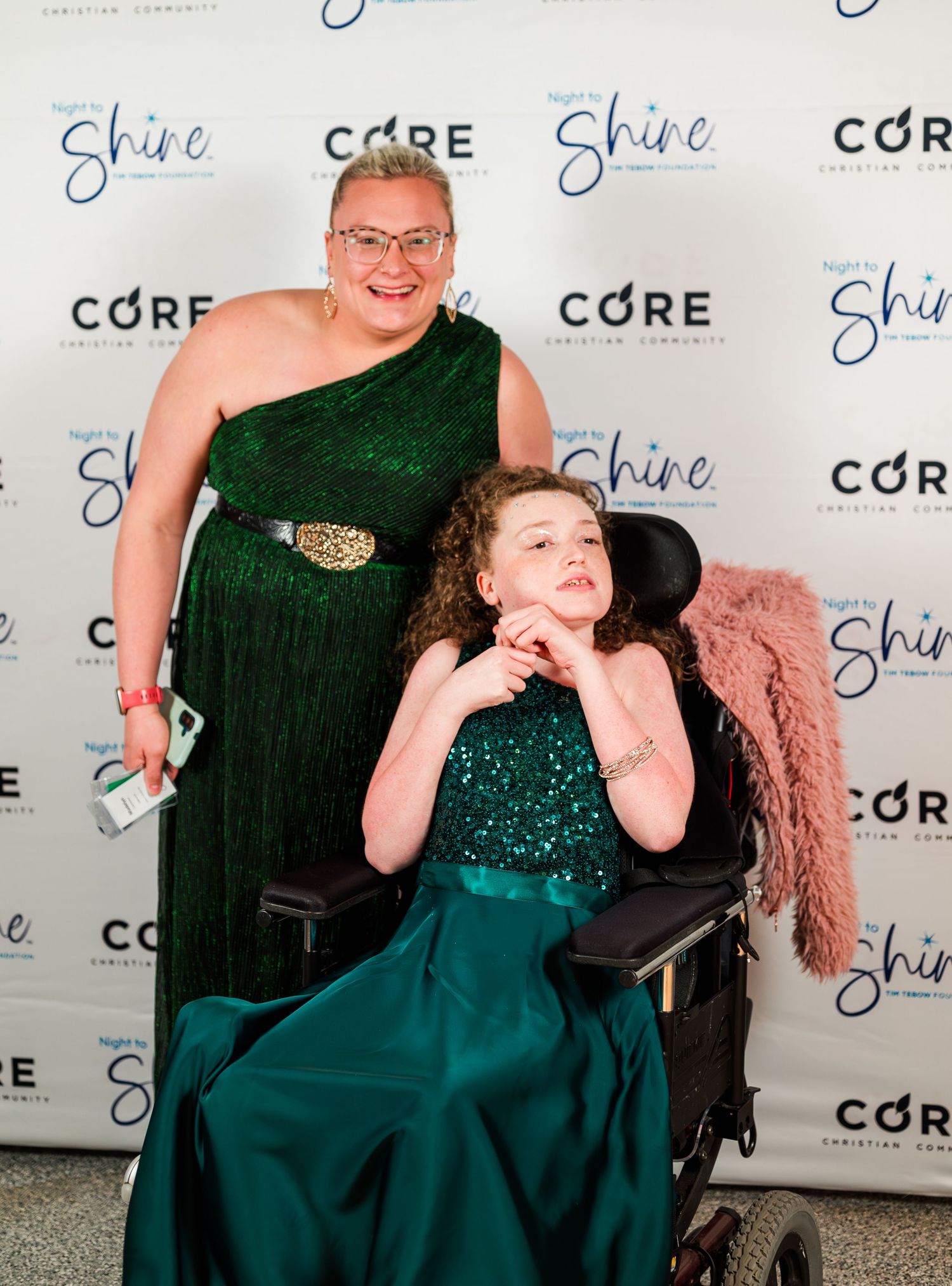 Guest in a wheelchair poses with volunteer at Night to Shine, dressed in elegant green, celebrating dignity, beauty, and inclusive community