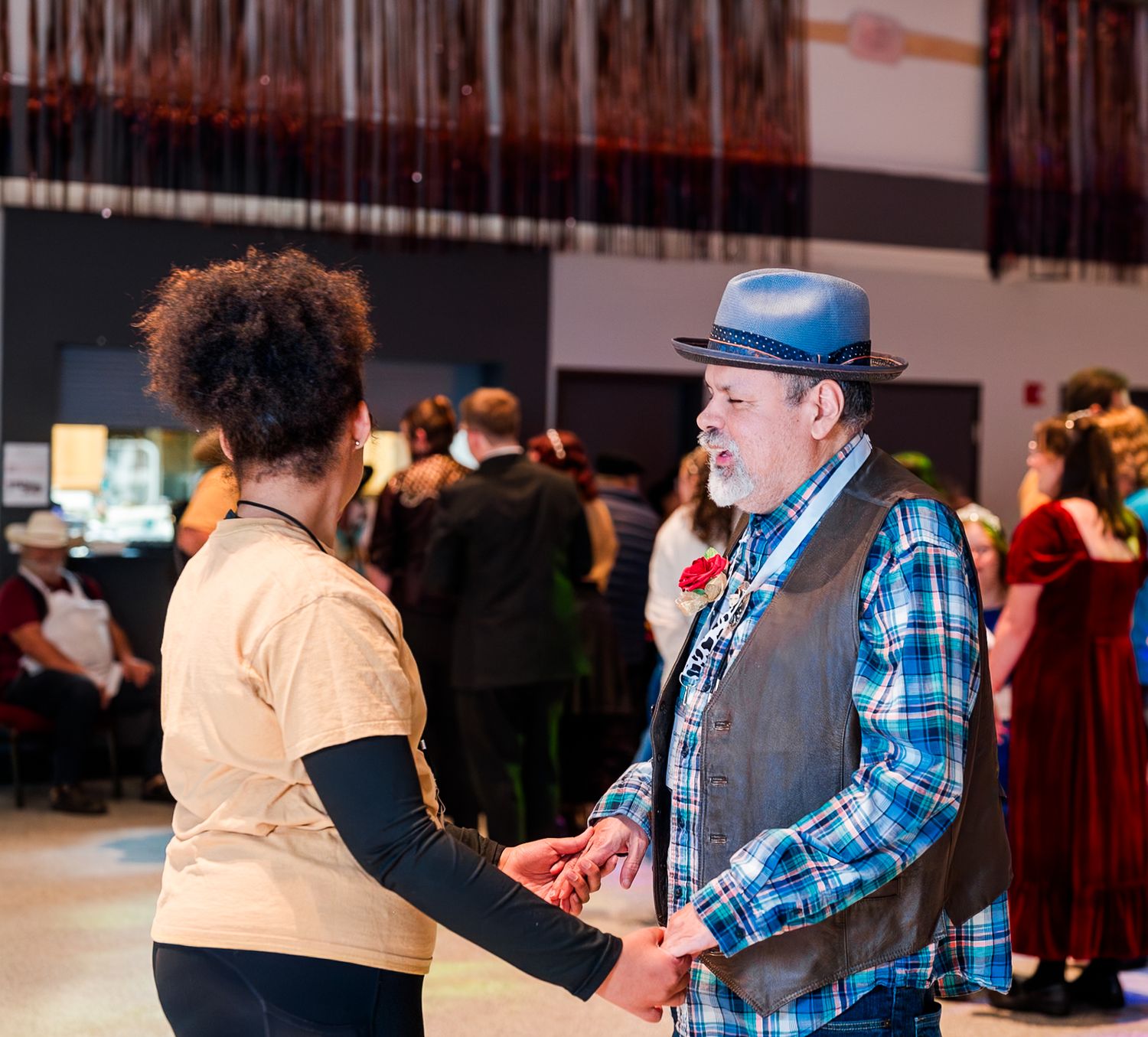 Guest and volunteer share a dance at Night to Shine, holding hands on the dance floor, celebrating joy, connection, and inclusive community.