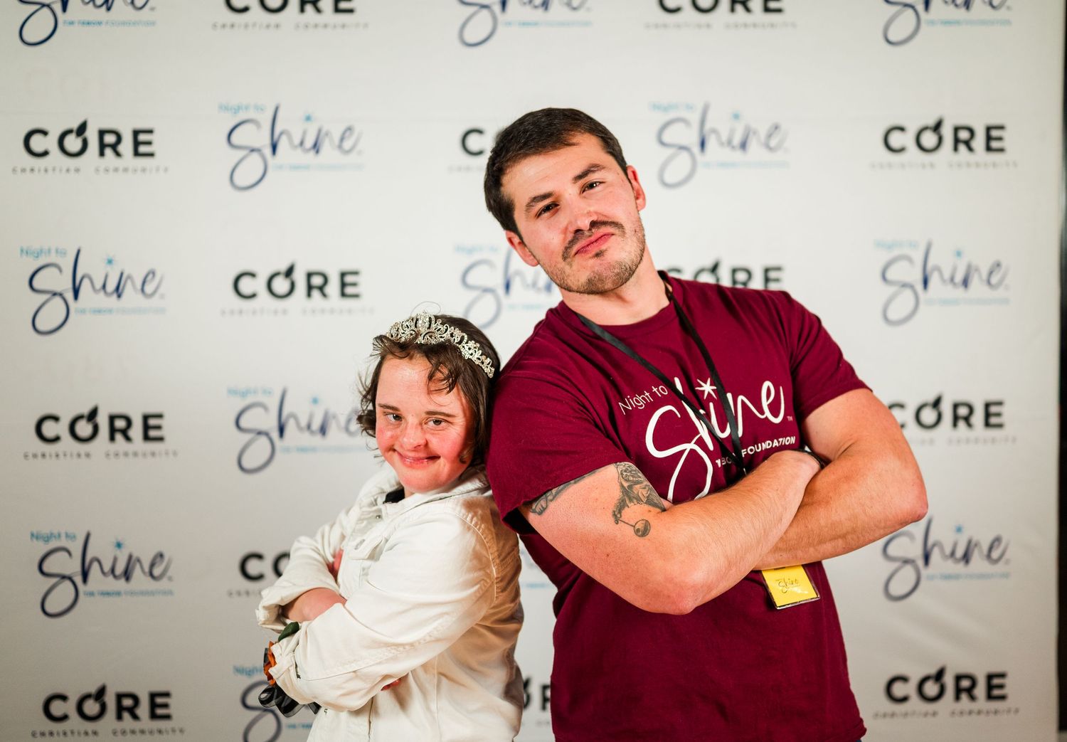 Guest and volunteer pose back-to-back at Night to Shine, smiling with confidence in front of event backdrop, celebrating joy, inclusion, and