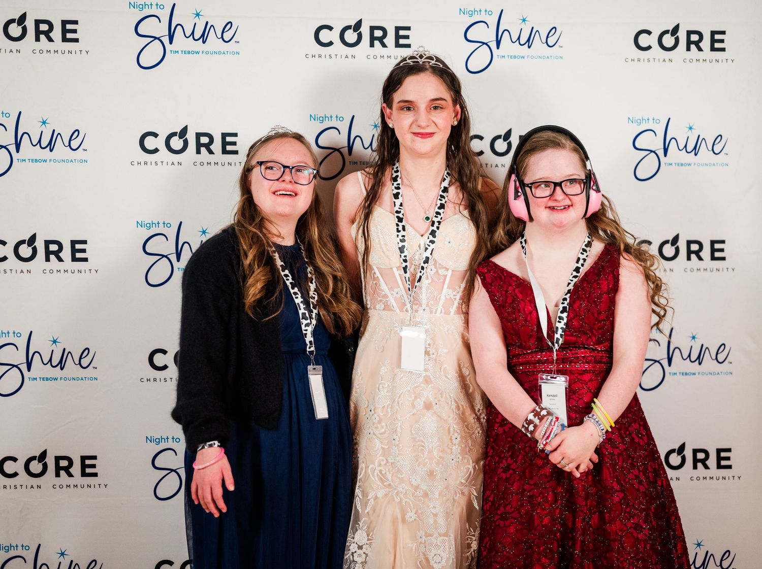 Three guests posing at Night to Shine event, dressed in formal gowns, capturing a joyful, inclusive celebration with confidence and friendsh