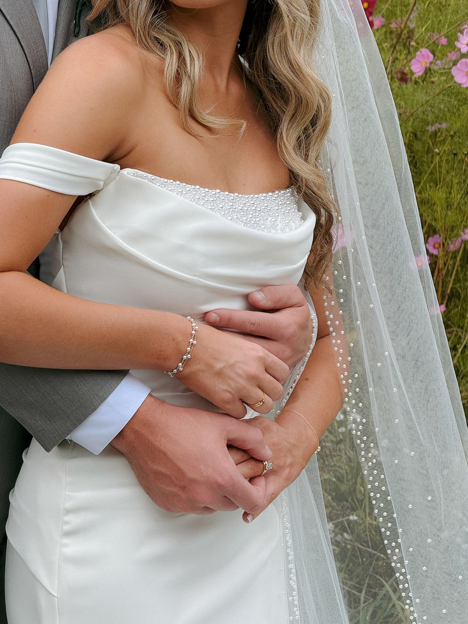 Close-up of newlyweds embracing, showing wedding dress details and rings.