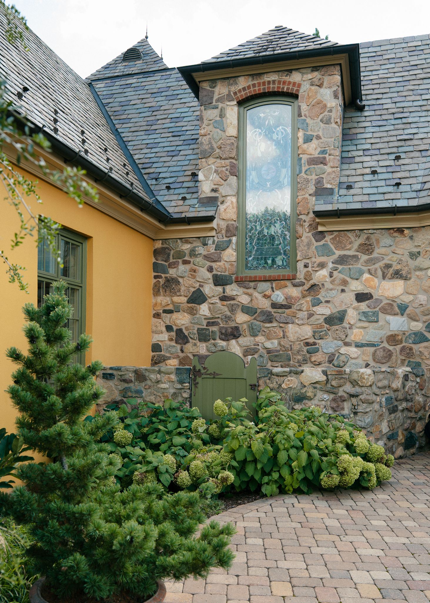 Stone and yellow stucco house exterior with tall windows and lush garden landscaping.