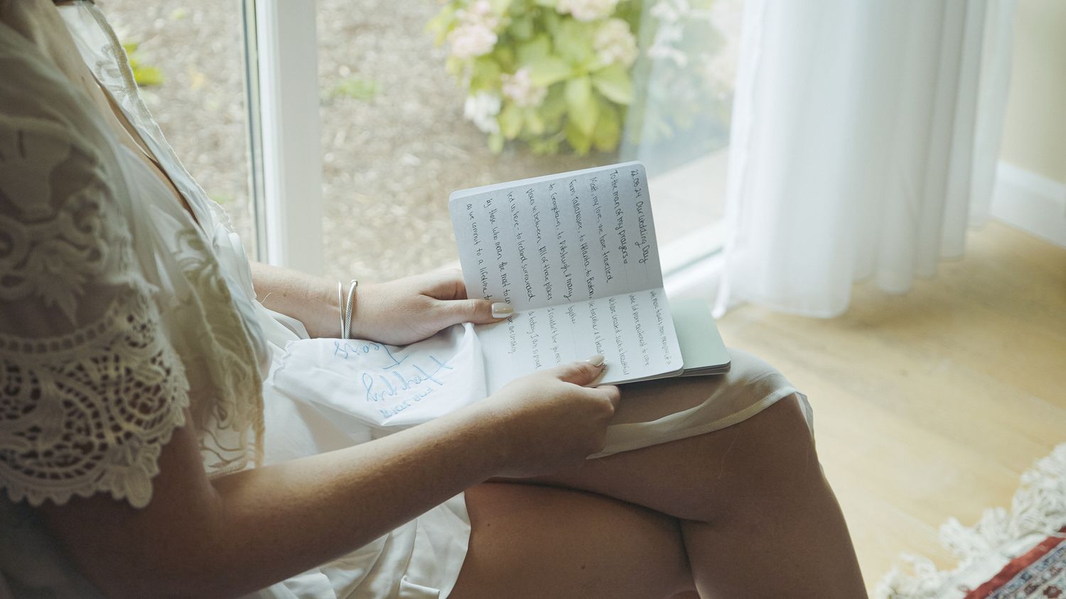 Someone reading a book by a bright window with white curtains and lace details.