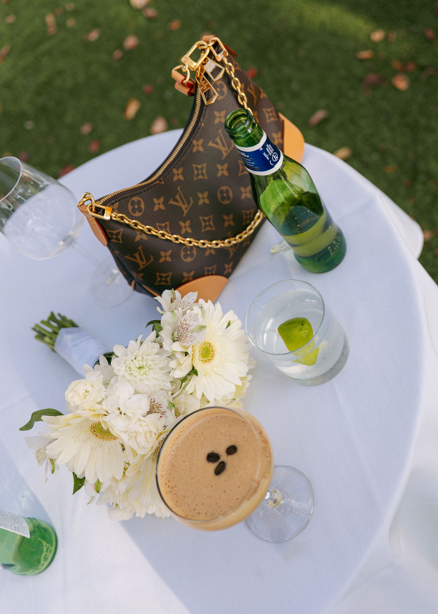 Designer handbag and white flowers arranged on outdoor table setting.